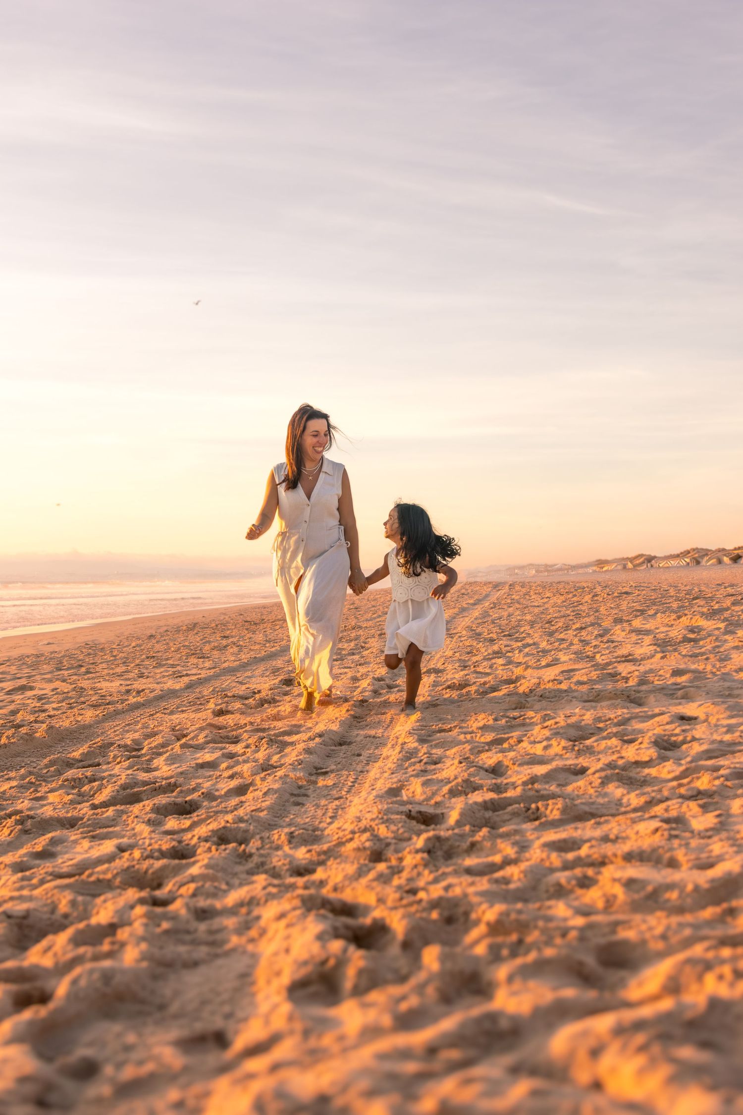 A person and a dog play together on a sandy beach at sunset with warm golden light illuminating the scene.