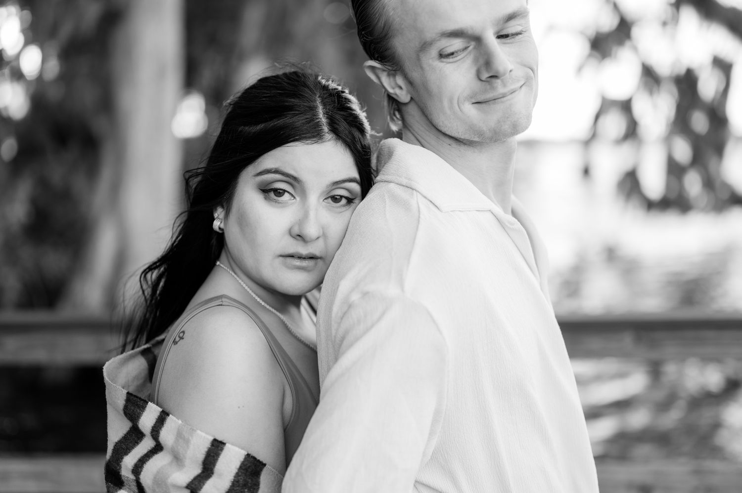 A romantic black and white portrait of a couple embracing outdoors with soft natural lighting.