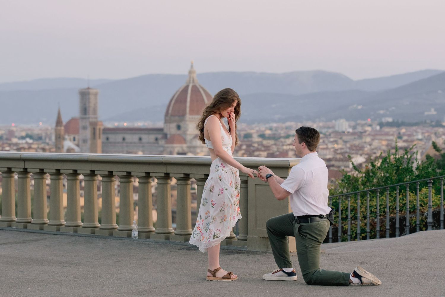 Man proposes to woman on one knee at Piazzale Michelangelo with Florence skyline and Duomo at sunset.
