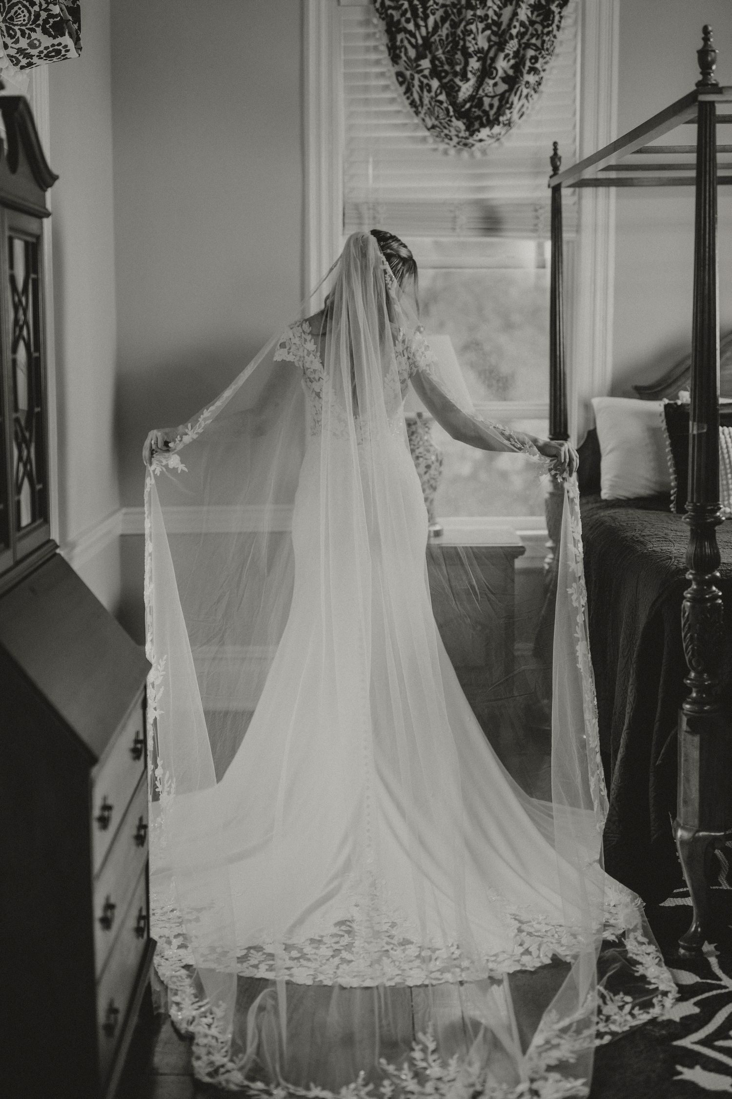 Elegant bride in lace wedding dress poses gracefully on a white porch, with soft bokeh lights in the background.