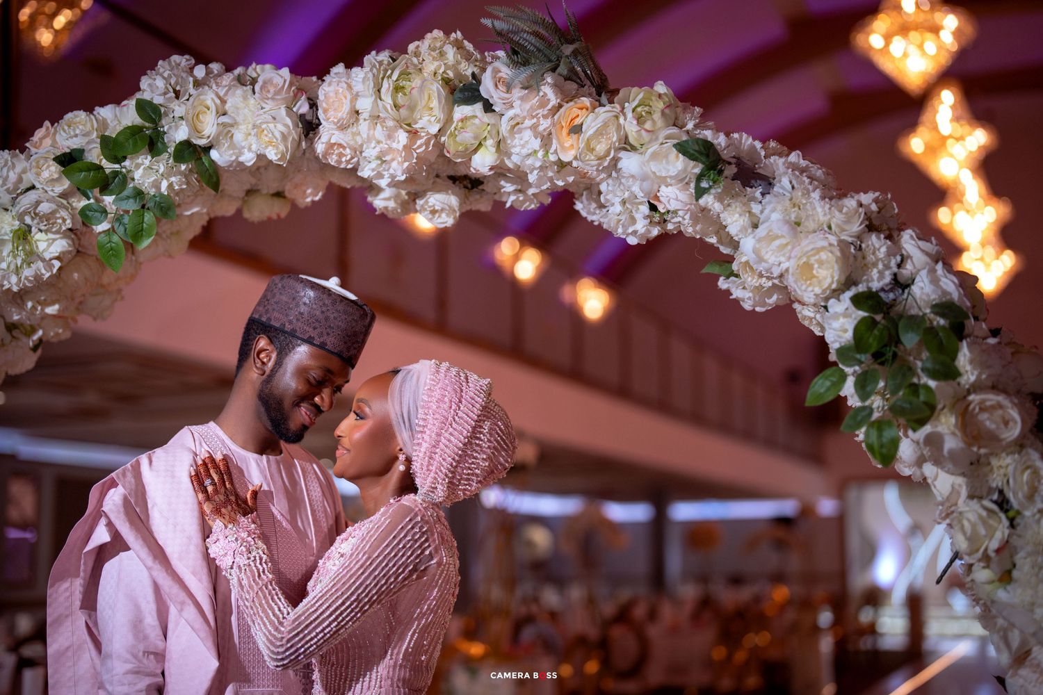 A romantic venue at dusk with white floral decor, glowing string lights, and couples sharing tender moments on the dance floor.