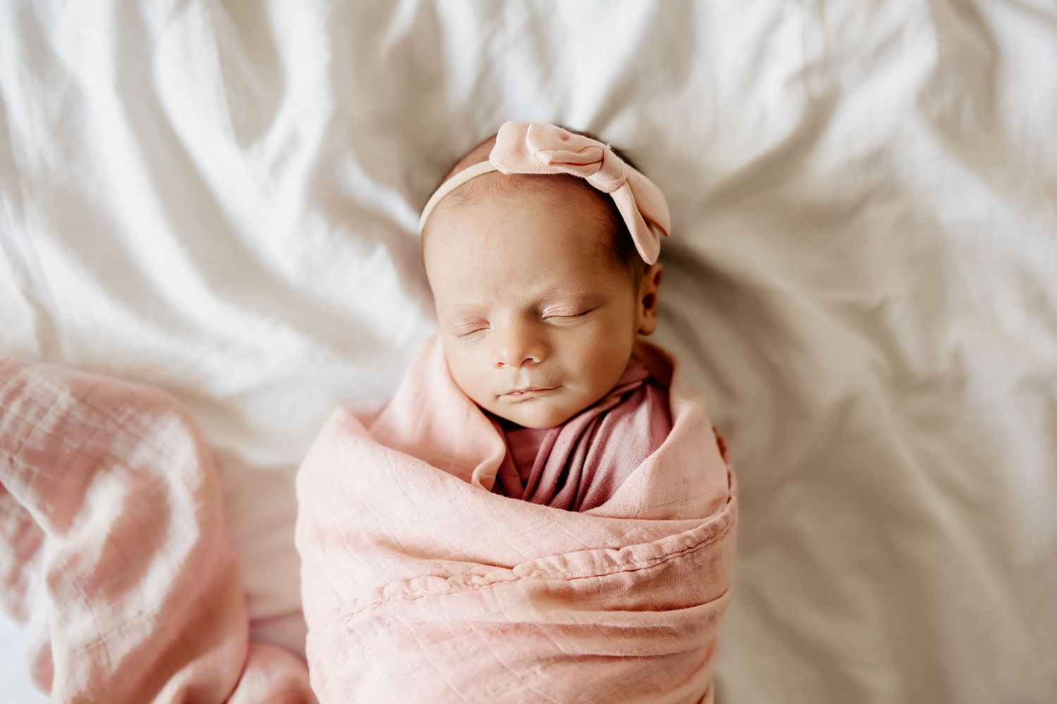 A newborn baby girl wrapped in a pink swaddle sleeping during her newborns session with an Oahu Newborn Photographer.