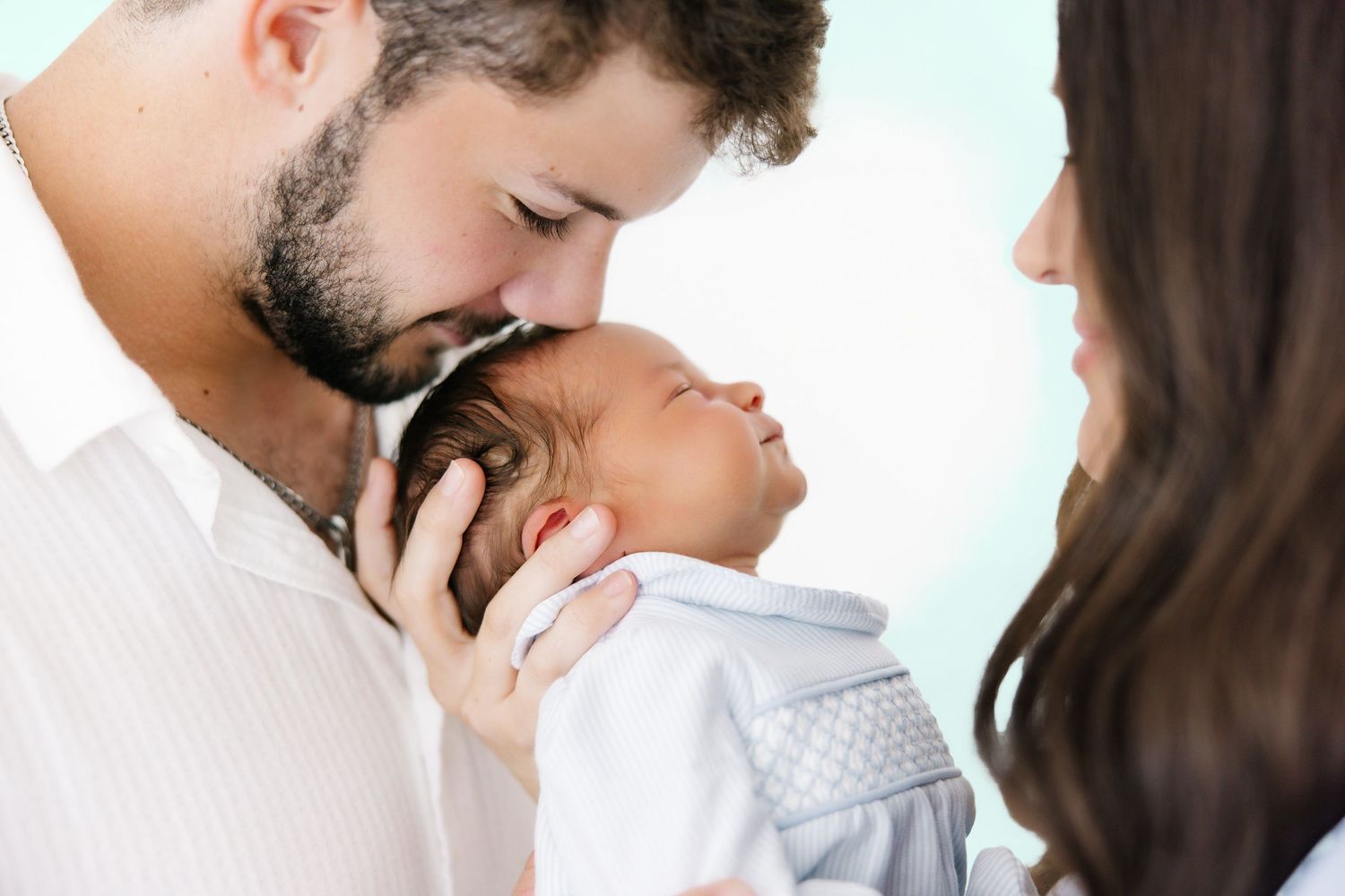 A tender moment between parents and their sleeping newborn baby wearing white clothing.