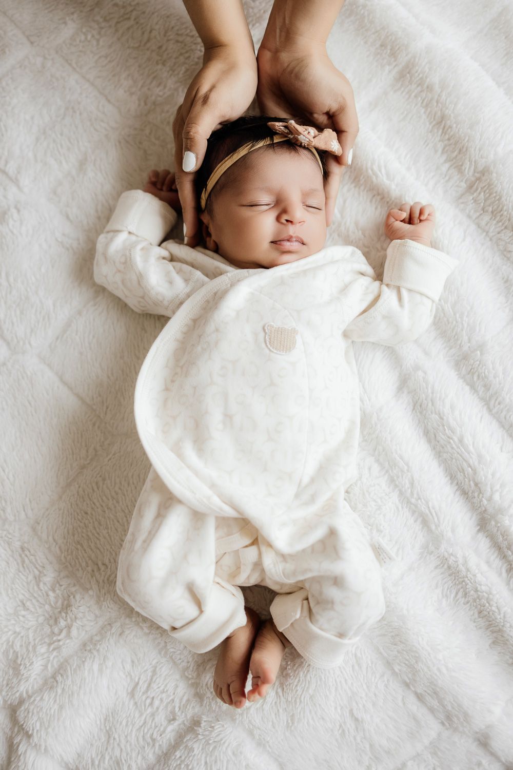 A newborn baby sleeps with her head cradled by mom's hands during her newborn photoshoot in San Jose