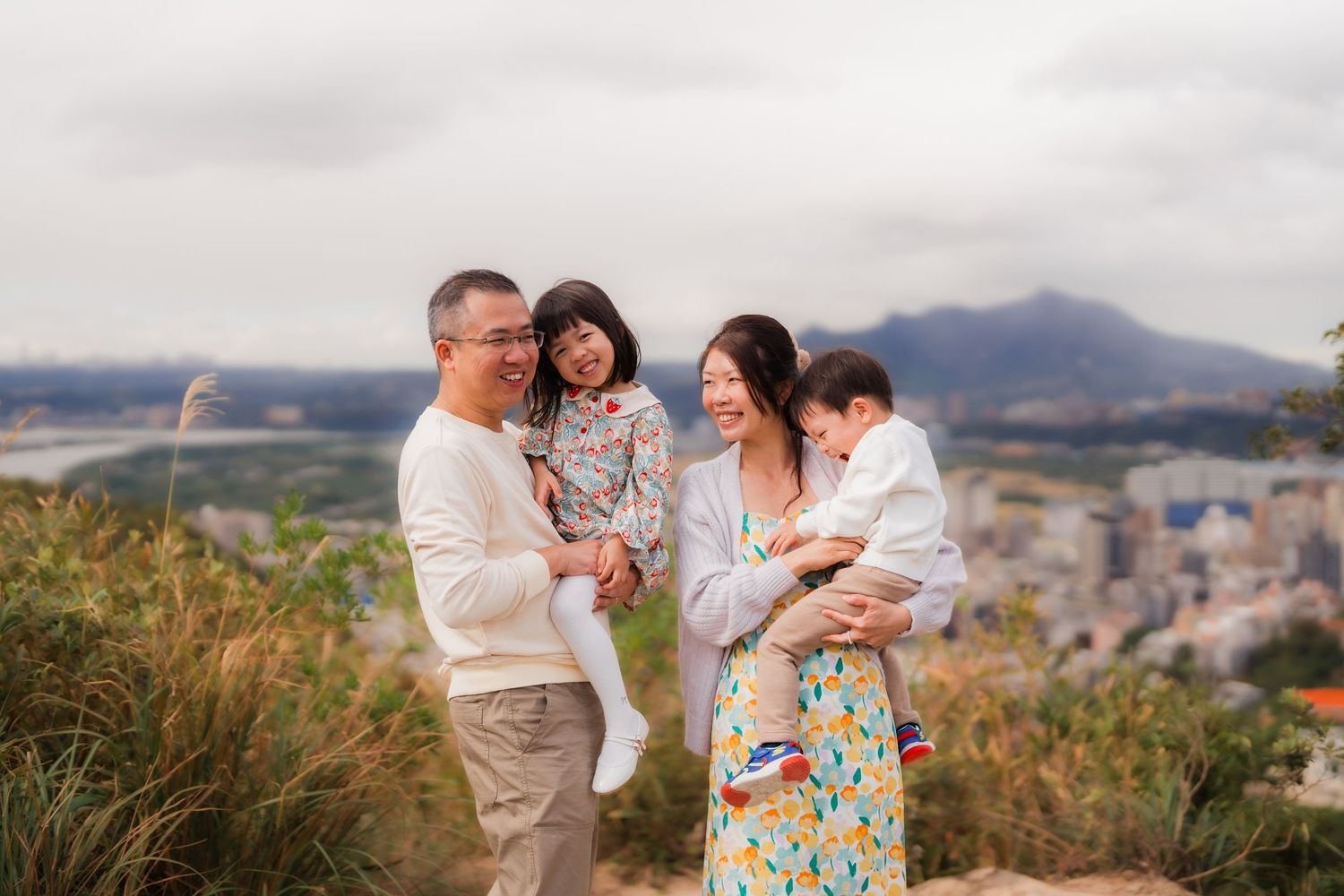 Family enjoying a scenic mountaintop view overlooking a city landscape on a cloudy day.