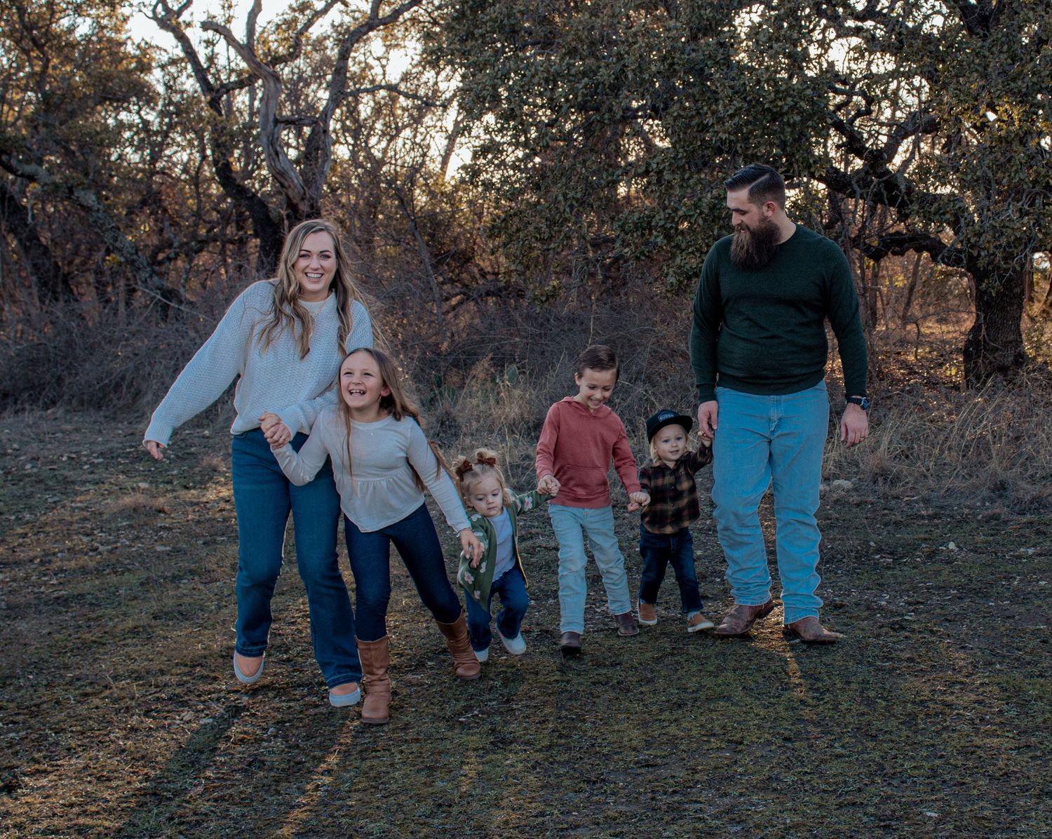Family members in blue jeans walk together through an outdoor setting at sunset.