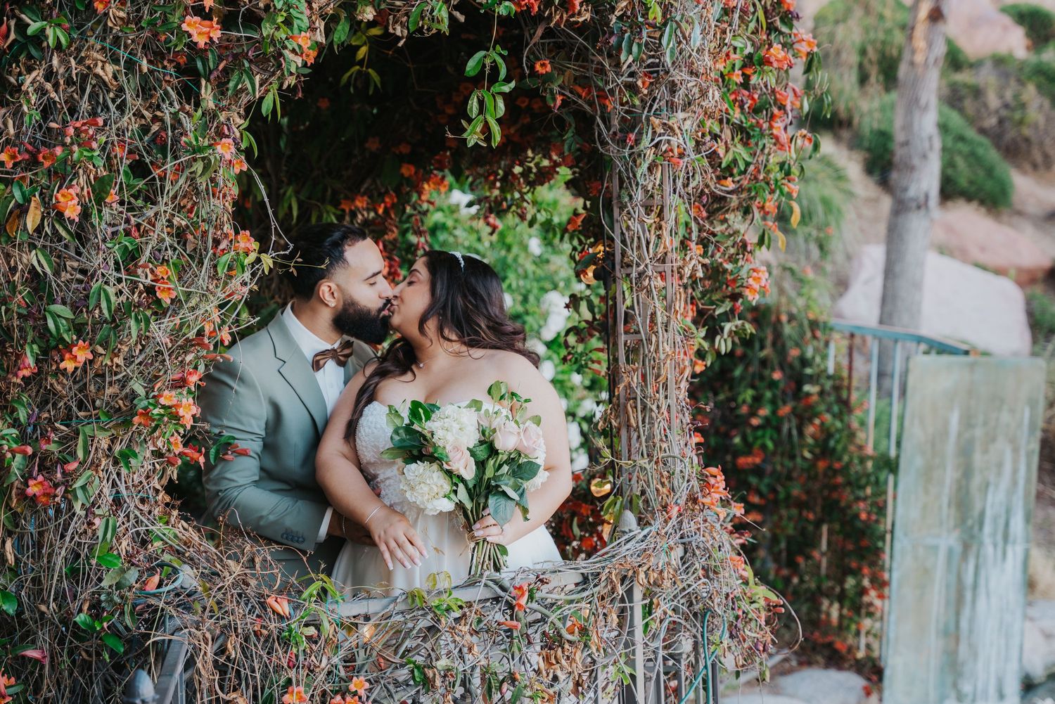 A romantic couple shares intimate moments under a blooming tree in a garden setting.