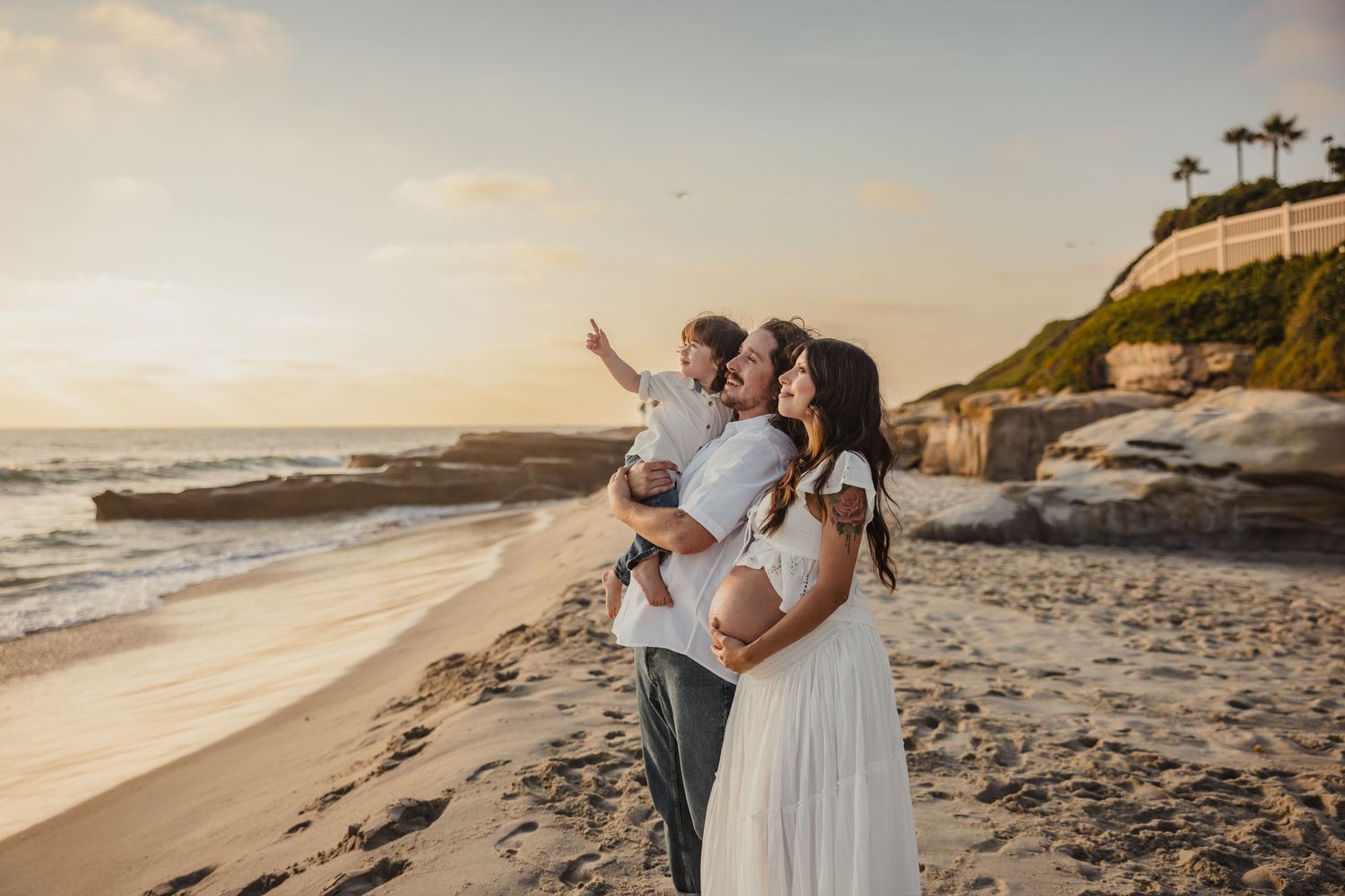 People stand together on a scenic beach at sunset with coastal cliffs and palm trees in the background.