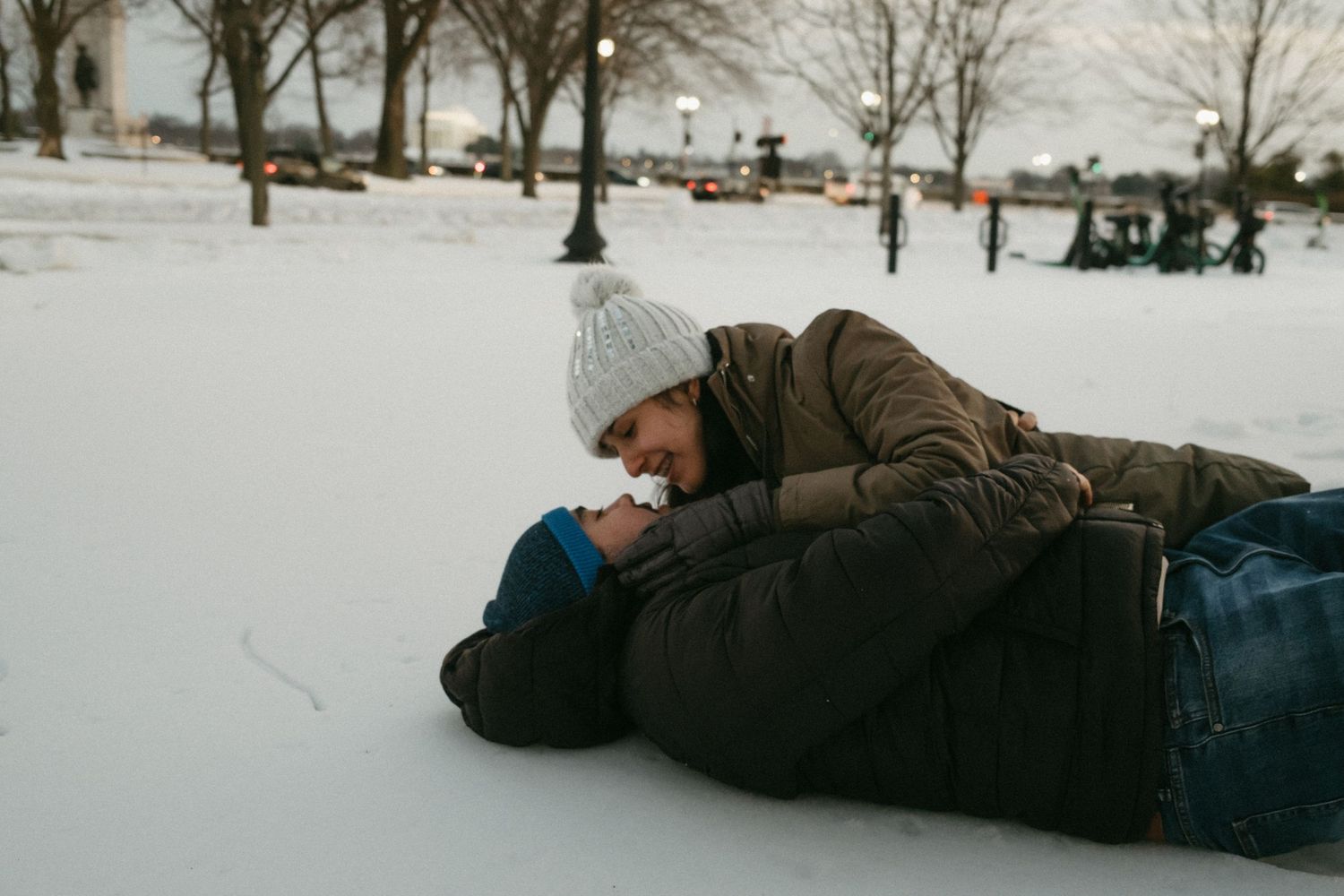 Two people lying in the snow together on a winter day, creating a romantic moment against a snowy landscape.