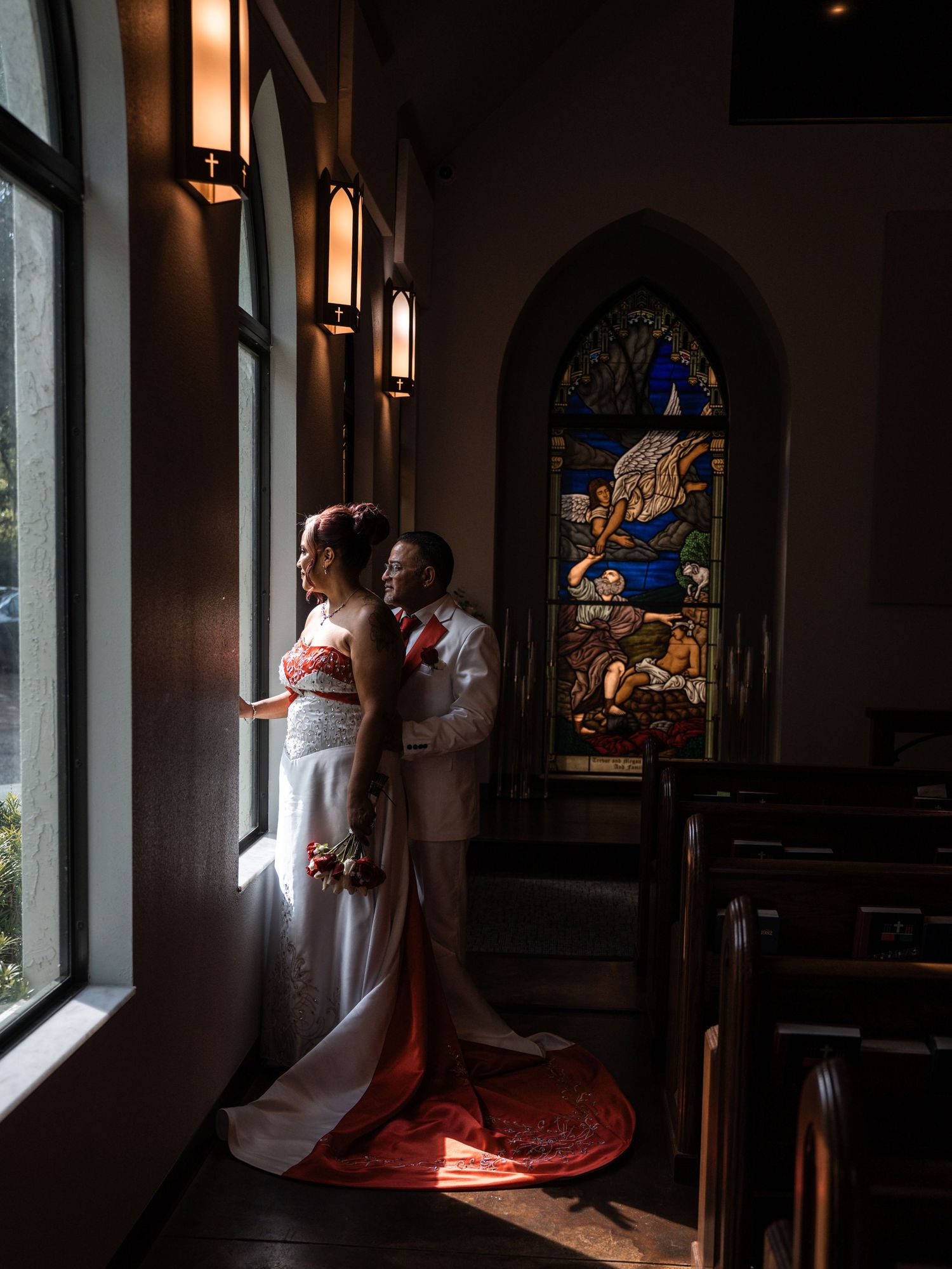Couple in elegant wedding attire standing by sunlit church windows creating dramatic silhouettes and lighting effects in Tampa Florida