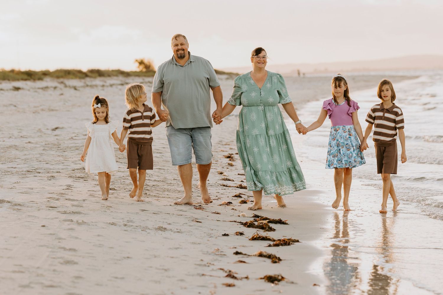 Family walking together along a scenic beach at sunset with waves crashing on the shore.