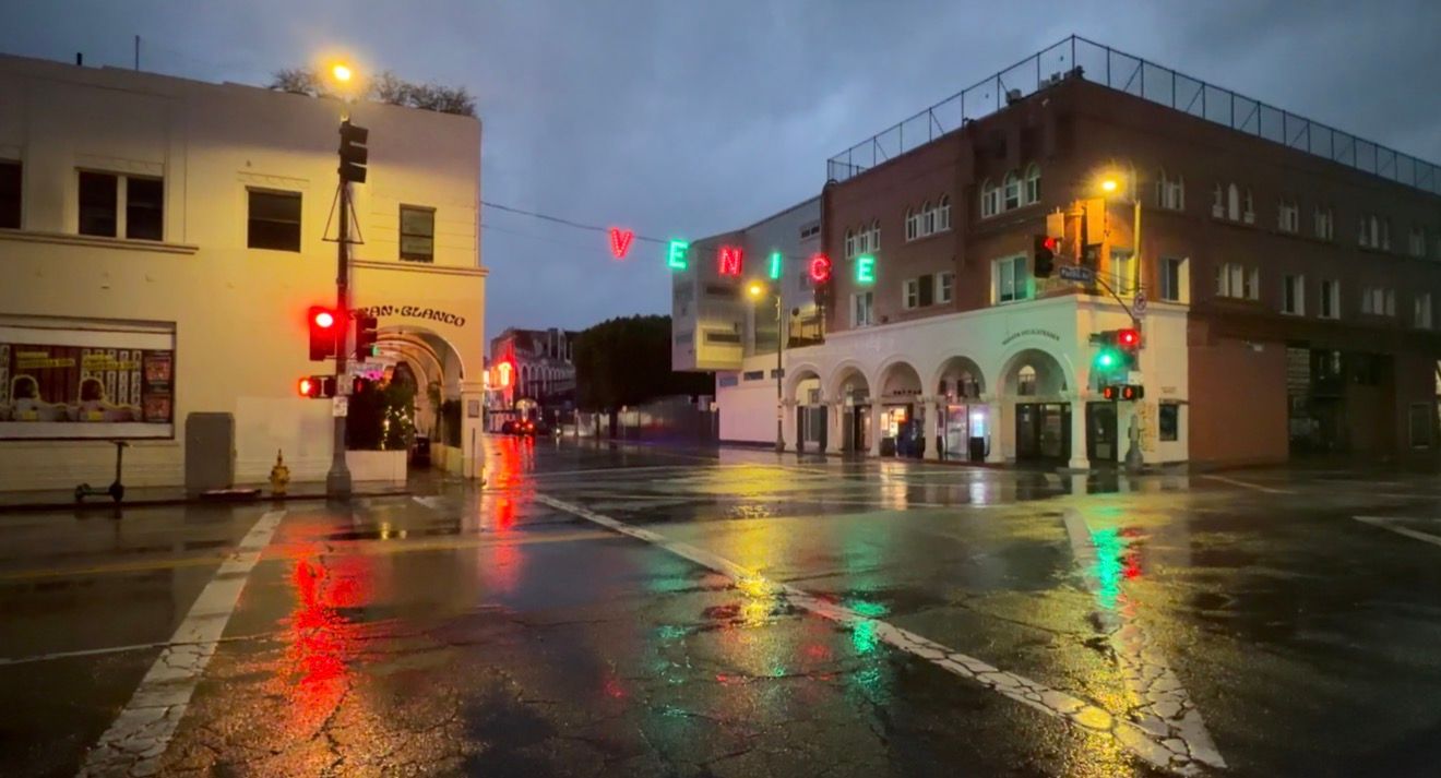 Rainy night street scene with glowing traffic lights reflecting on wet pavement in an urban area.