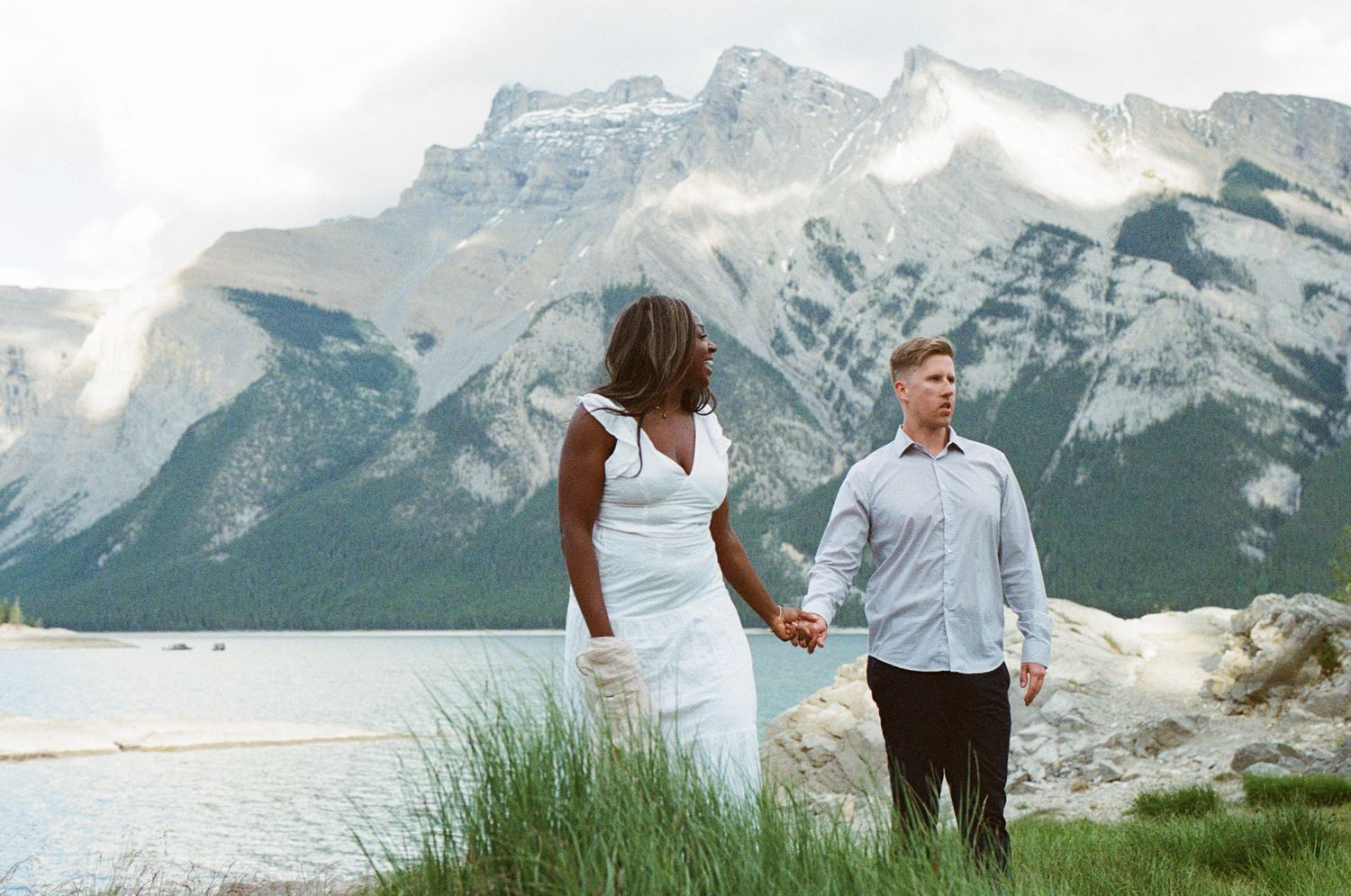 35 mm film photo of bride and groom laughing on the shore of Lake Minnewanka in Banff with Mount Inglismaldie in the background.