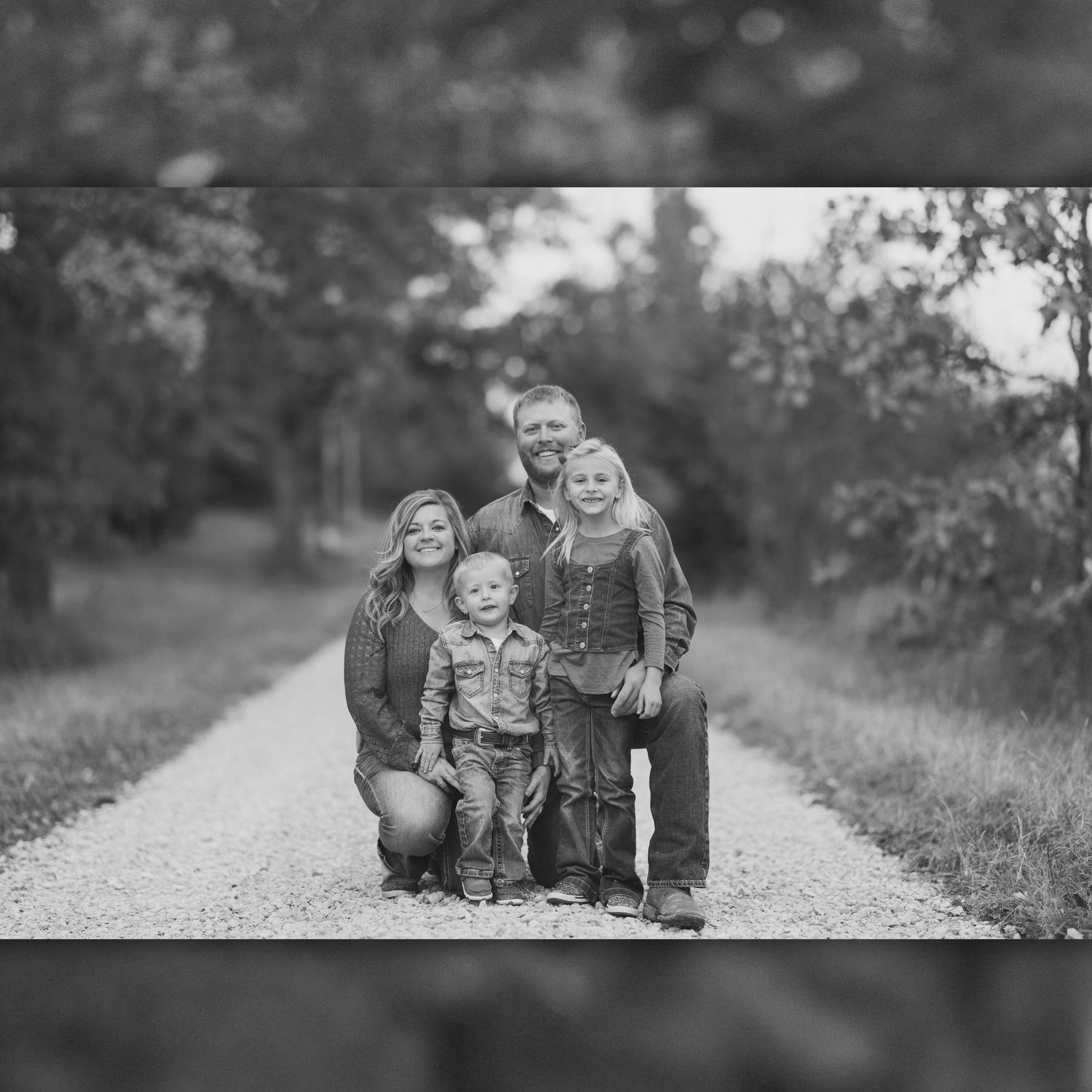 Black and white family portrait session on a rustic path through nature with soft lighting and natural poses.