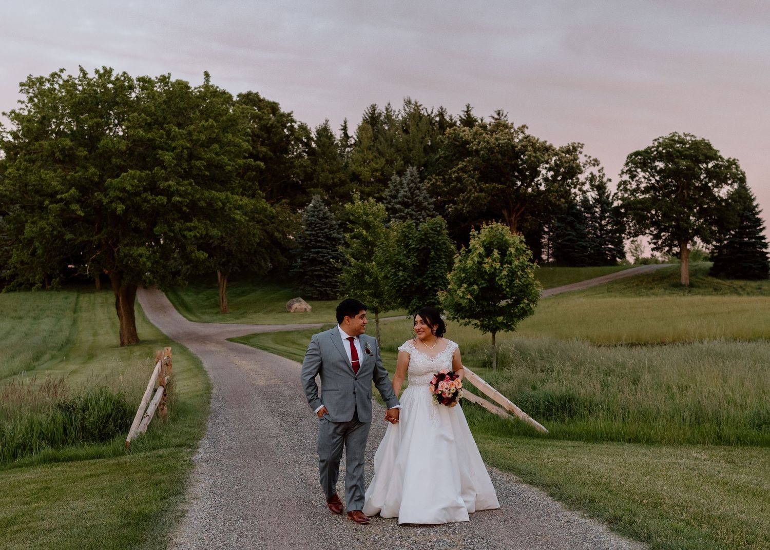 Wedding photography sequence showing couple walking along a rustic gravel path through rolling countryside fields at sunset.