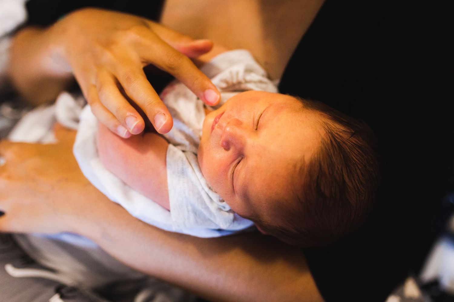 Newborn baby in white clothing lies peacefully while being cradled in someone's arms.