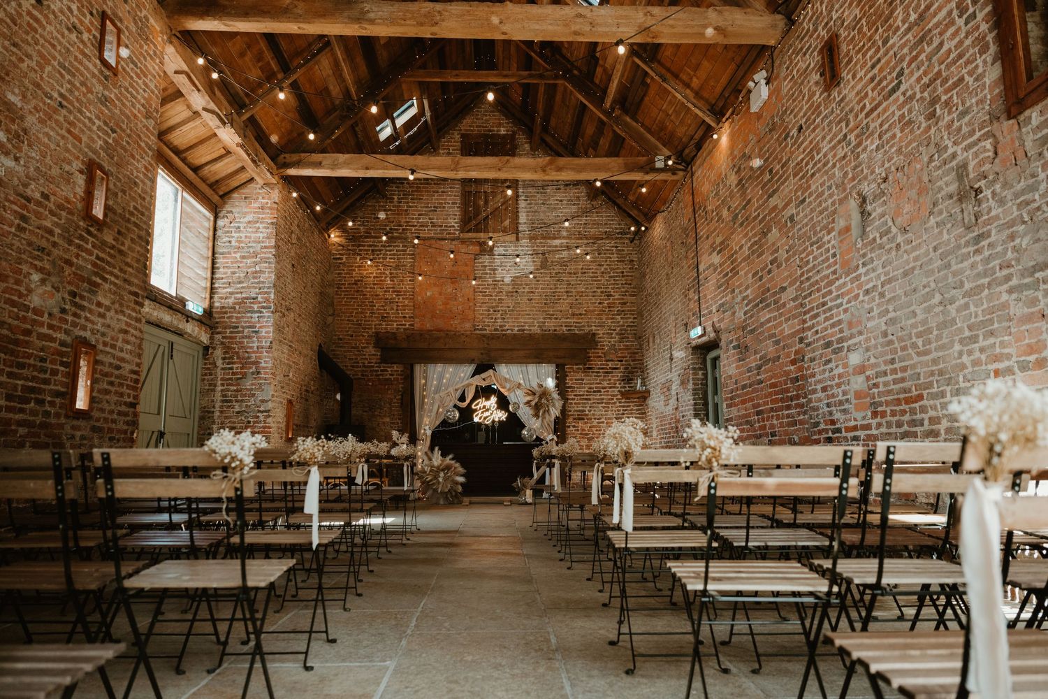 Riverlands. Panoramic view of a rustic brick barn venue with wooden tables and benches set up for an event.