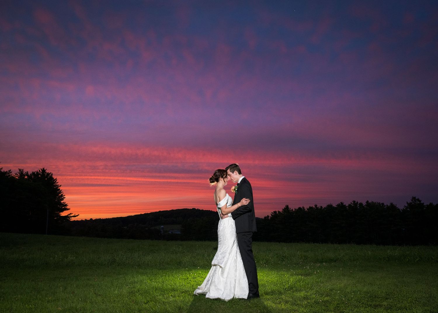 Newlyweds share an intimate moment outdoors with autumn foliage and rustic architecture in background.