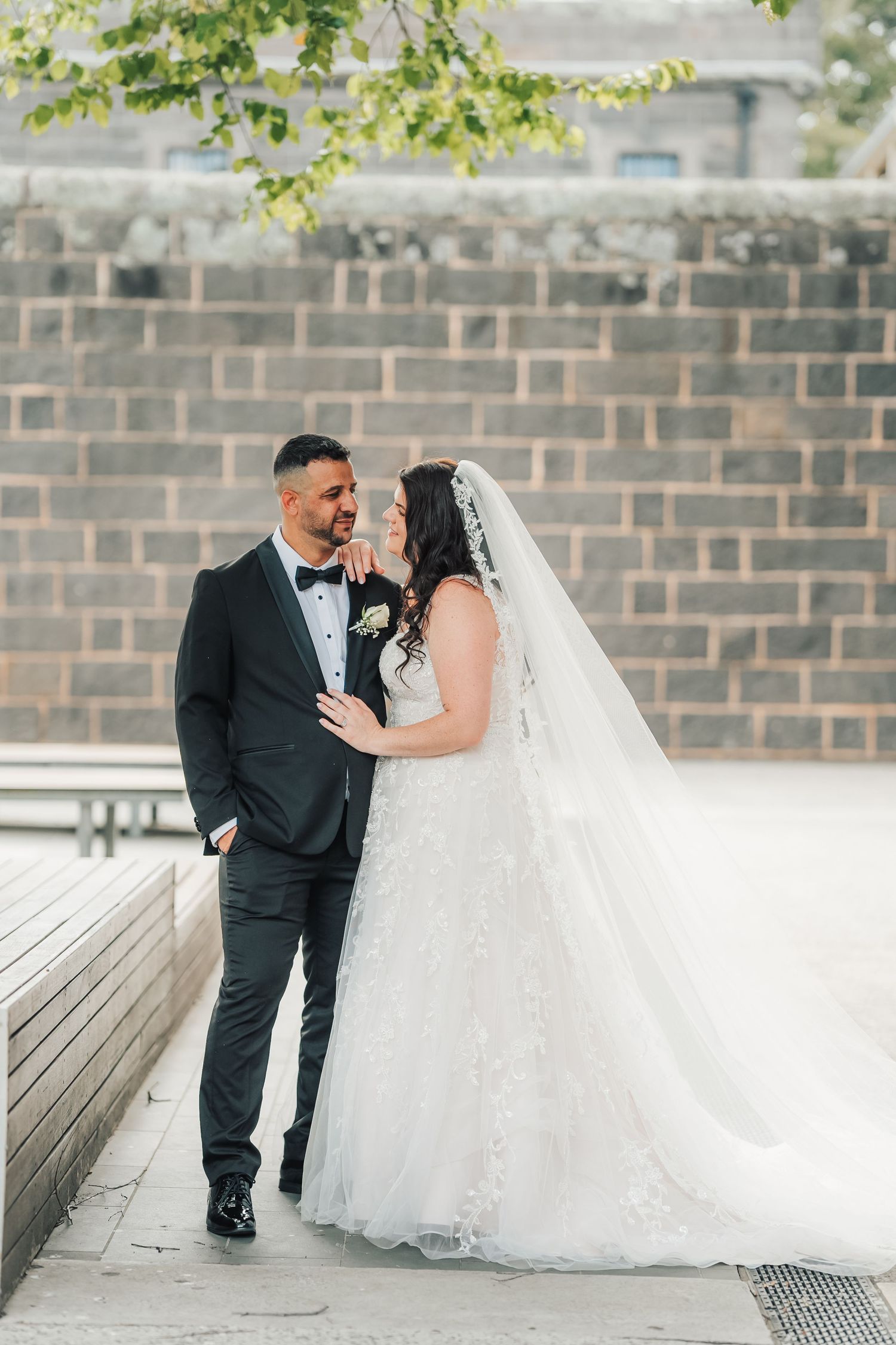 A happy newlywed couple shares romantic moments on a paver patio surrounded by greenery and brick walls.