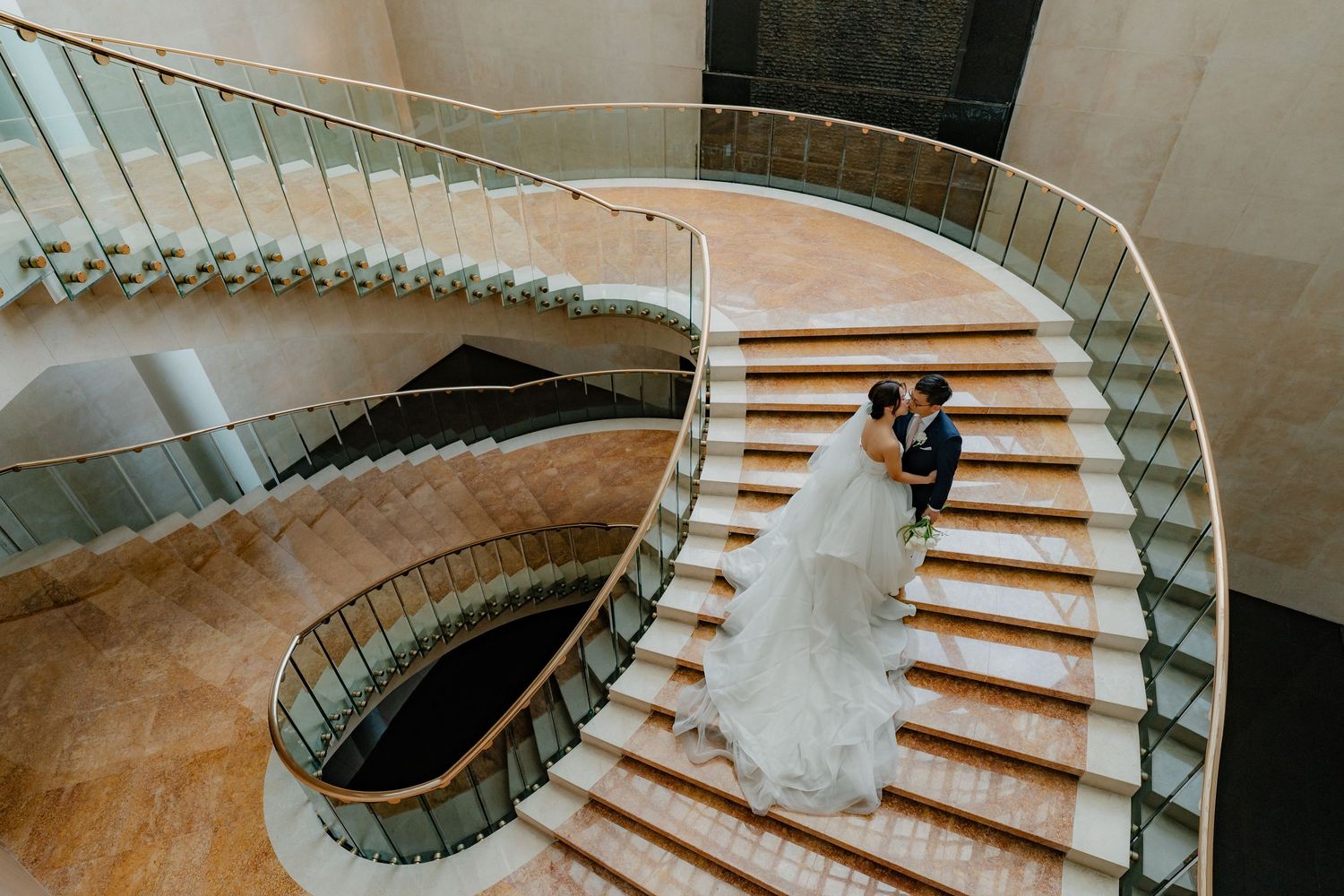 Aerial view of an elegant spiral staircase with curved metal railings and a couple in wedding attire standing on the steps.