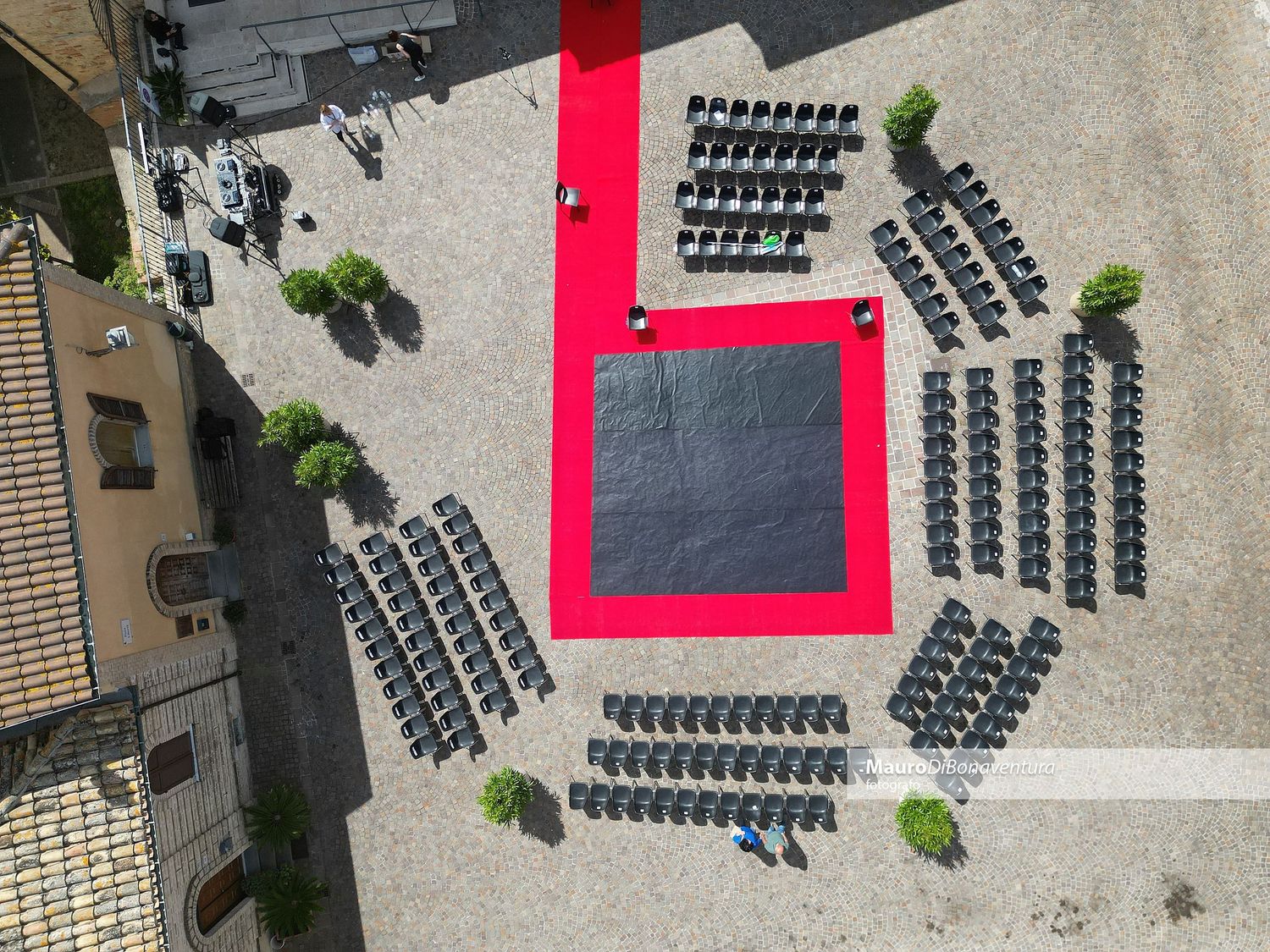 Aerial view of outdoor event setup with black chairs arranged in sections around a red carpet walkway.