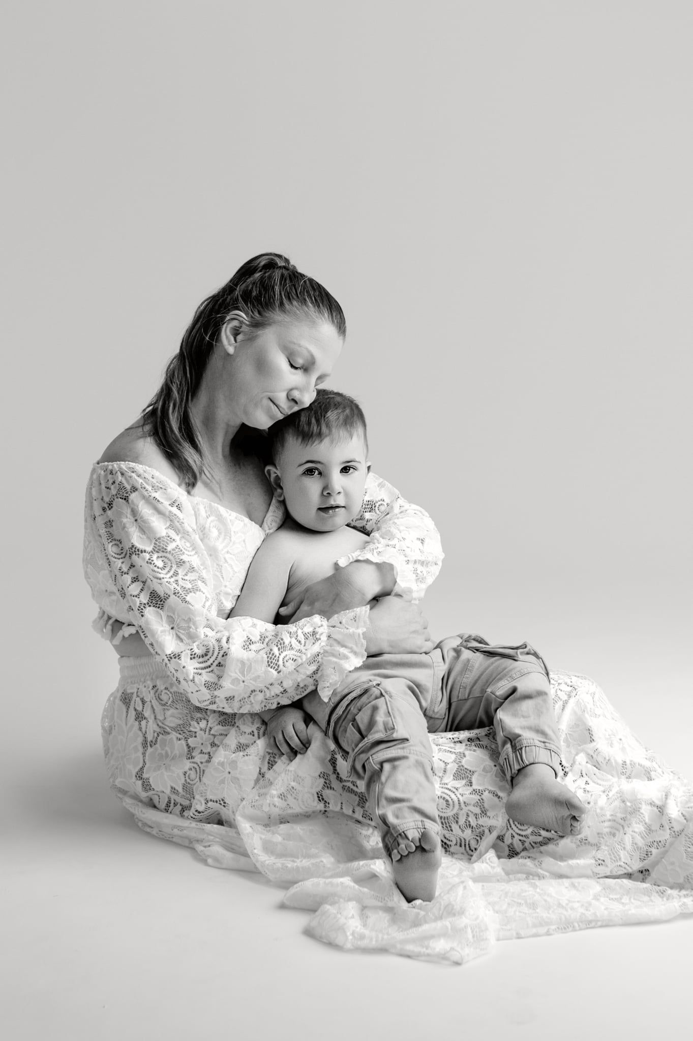 A tender black and white photo series showing a parent in white lace dress lying down and bonding with their baby.