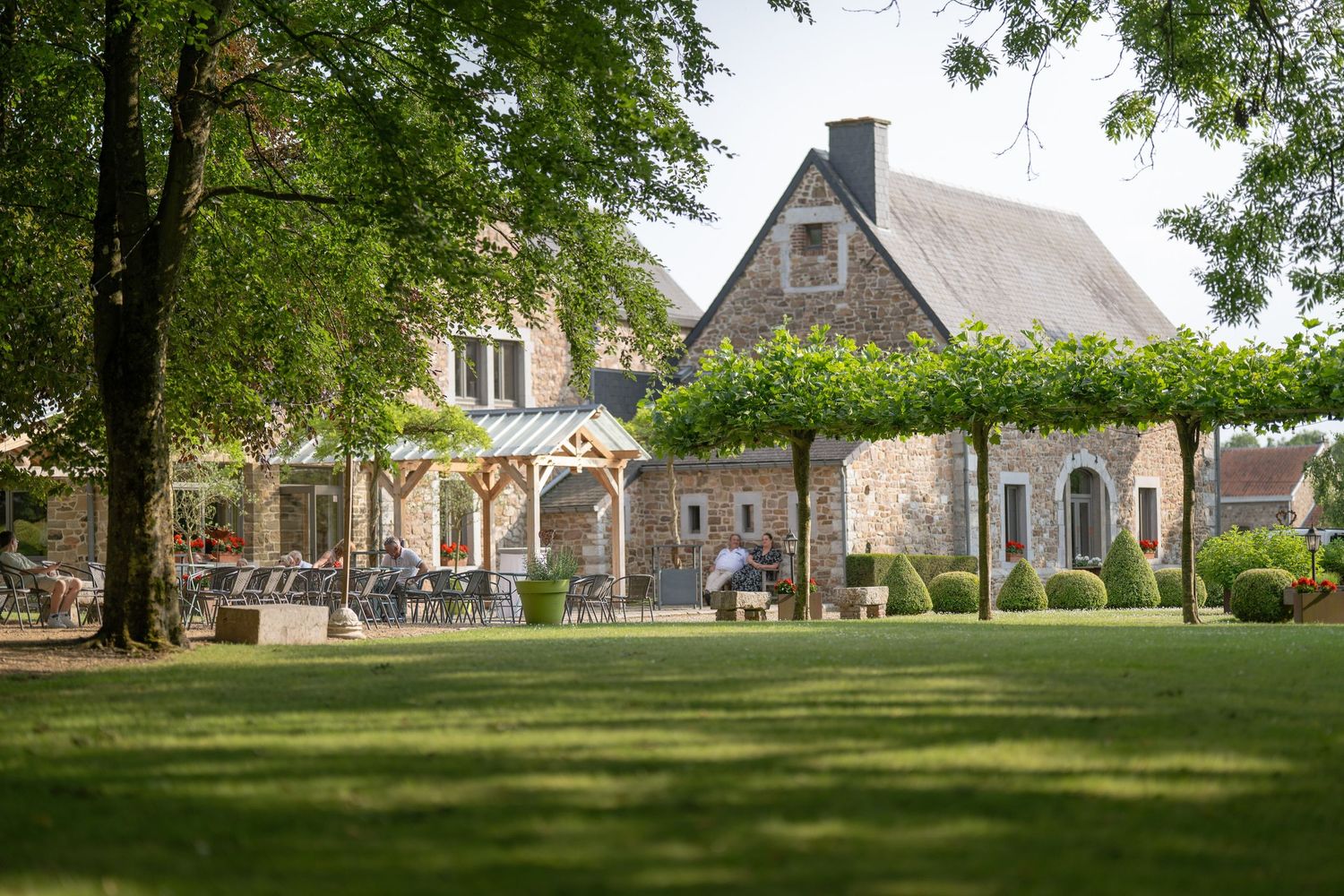 An expansive view of a stone church campus with green lawns and mature trees providing shade on a sunny day.