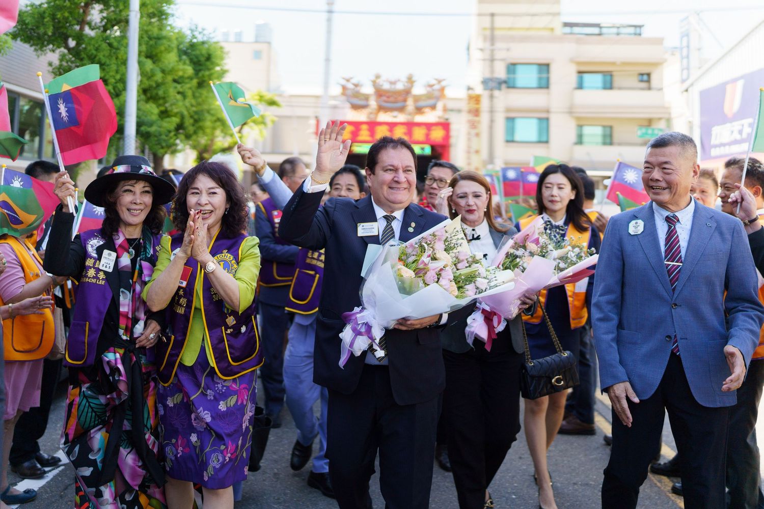 A group of people celebrating at an outdoor event with flowers and colorful traditional clothing.