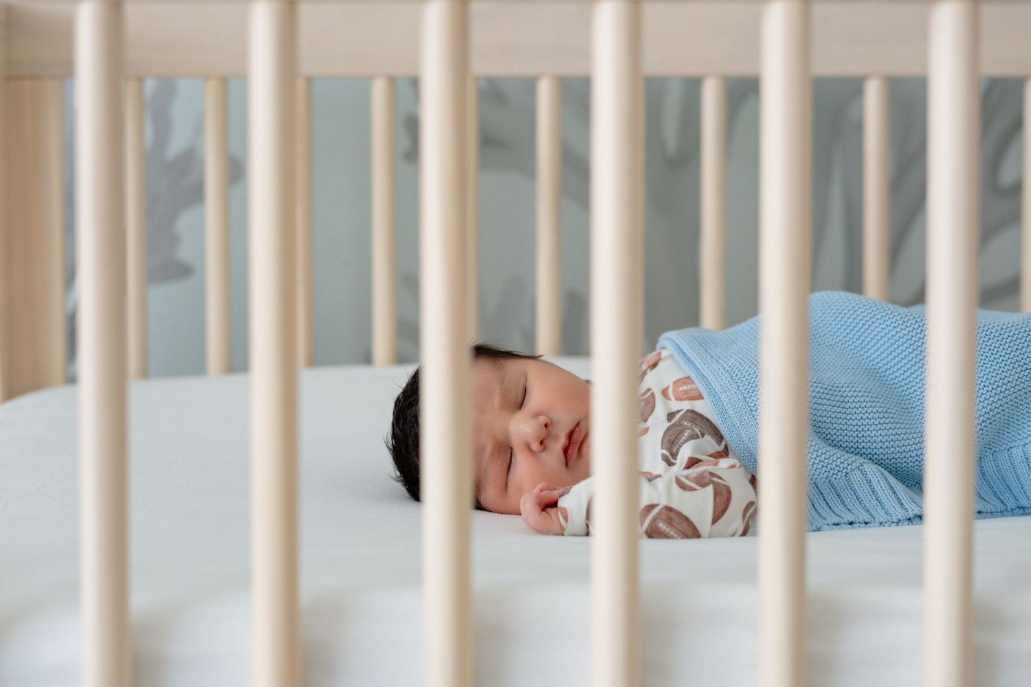 Newborn baby sleeping peacefully in a white wooden crib, swaddled in a soft blanket.
