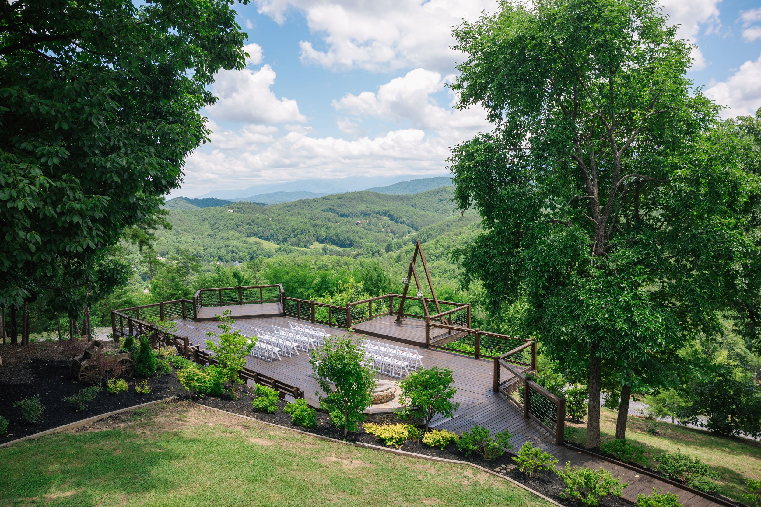 Scenic outdoor wedding venue with a wooden bridge, lush green trees, Scenic and stunning Tennessee mountain views under a partly cloudy sky.