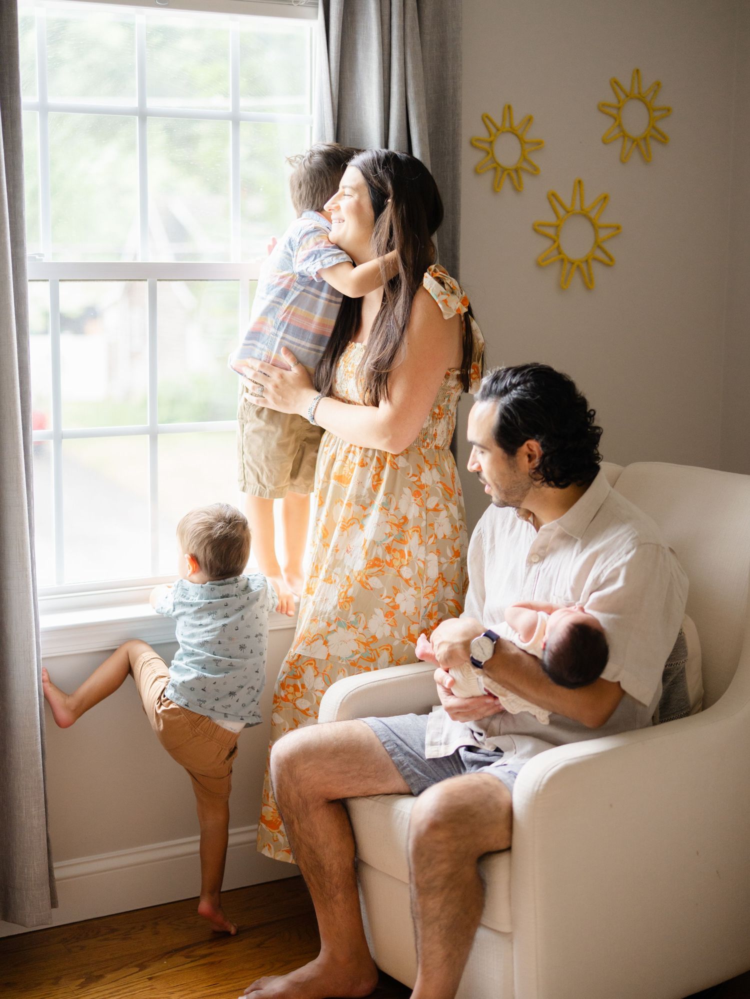 Mom holding big brother while dad snuggles newborn baby in natural window light during Ocean County NJ newborn photography session.