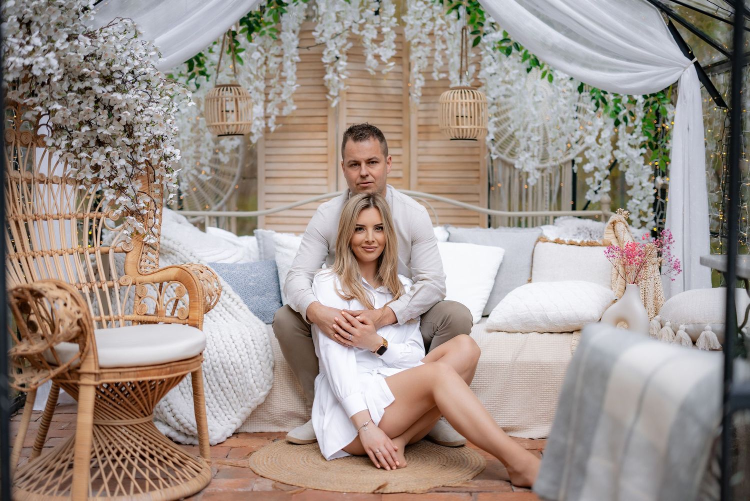 Couple relaxes together on white outdoor couch under floral archway.