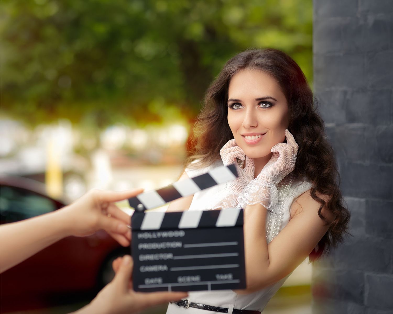 A movie scene being filmed with a clapperboard in front of a glamorous actress in evening wear.
