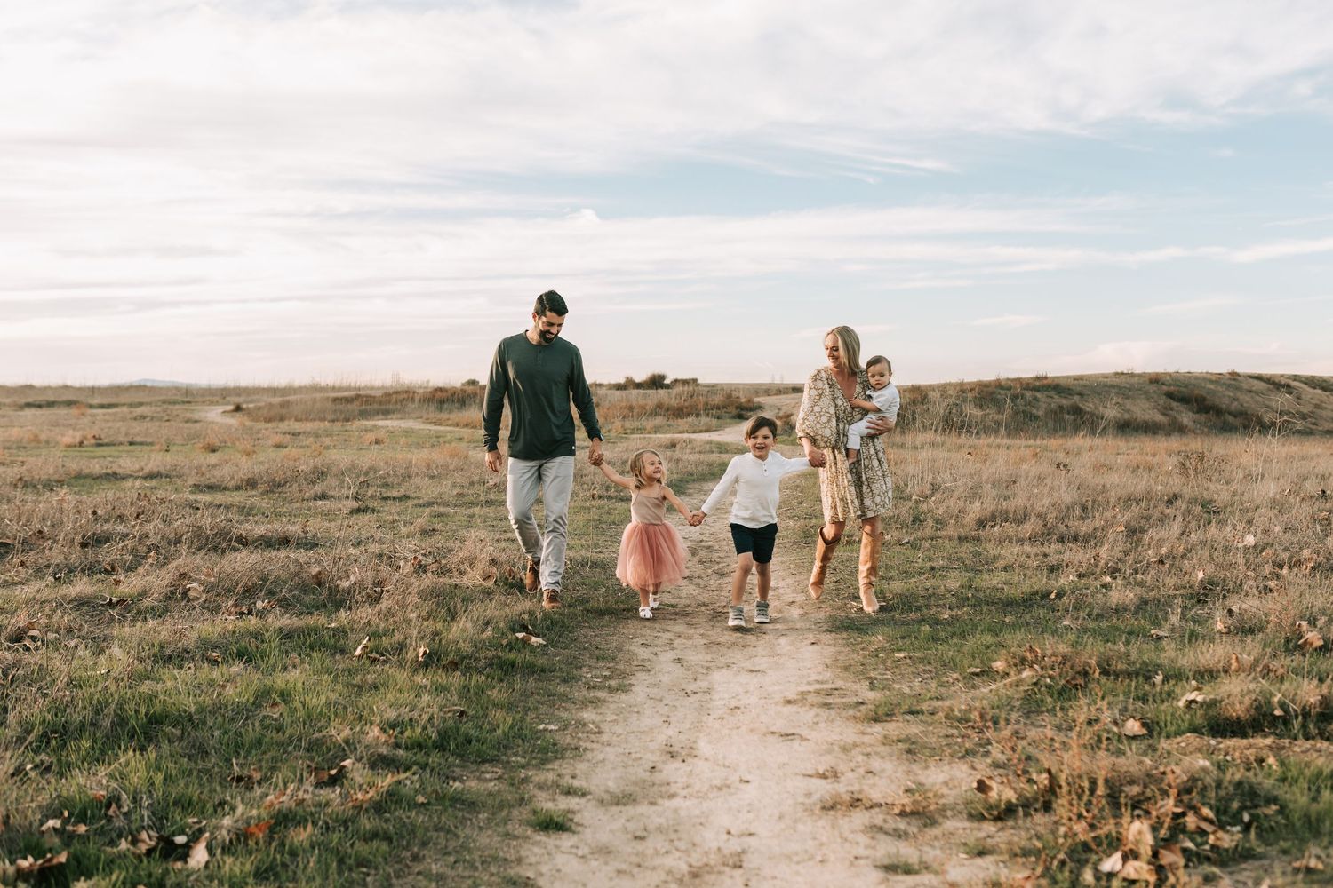 A group walks together along a winding dirt path through golden prairie grasslands at sunset.