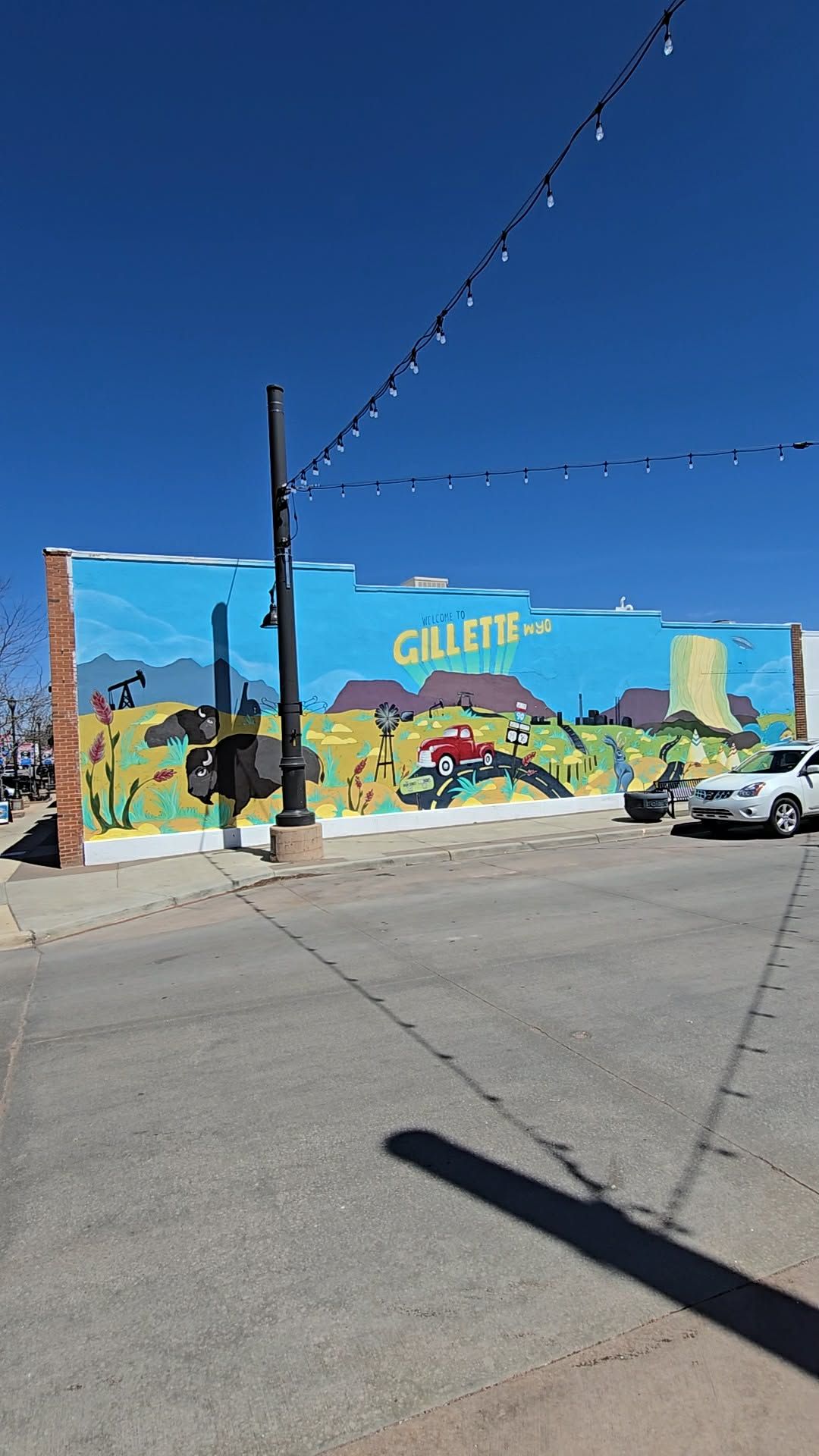 Colorful Gillette Wyoming mural on brick building featuring bison, red truck, and Devils Tower under a clear blue sky.
