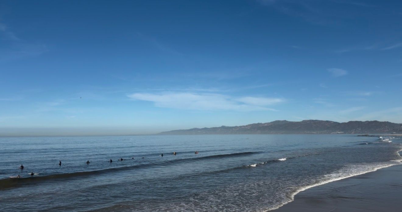 Calm ocean waves gently lap a sandy beach under a clear blue sky with distant mountains on the horizon.