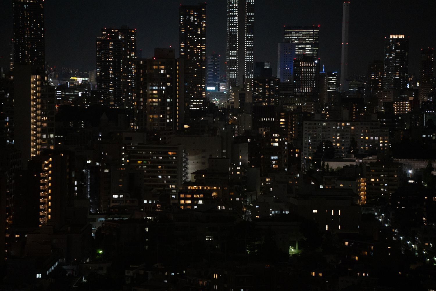 Nighttime cityscape with illuminated skyscrapers and apartment buildings glowing against a dark sky.