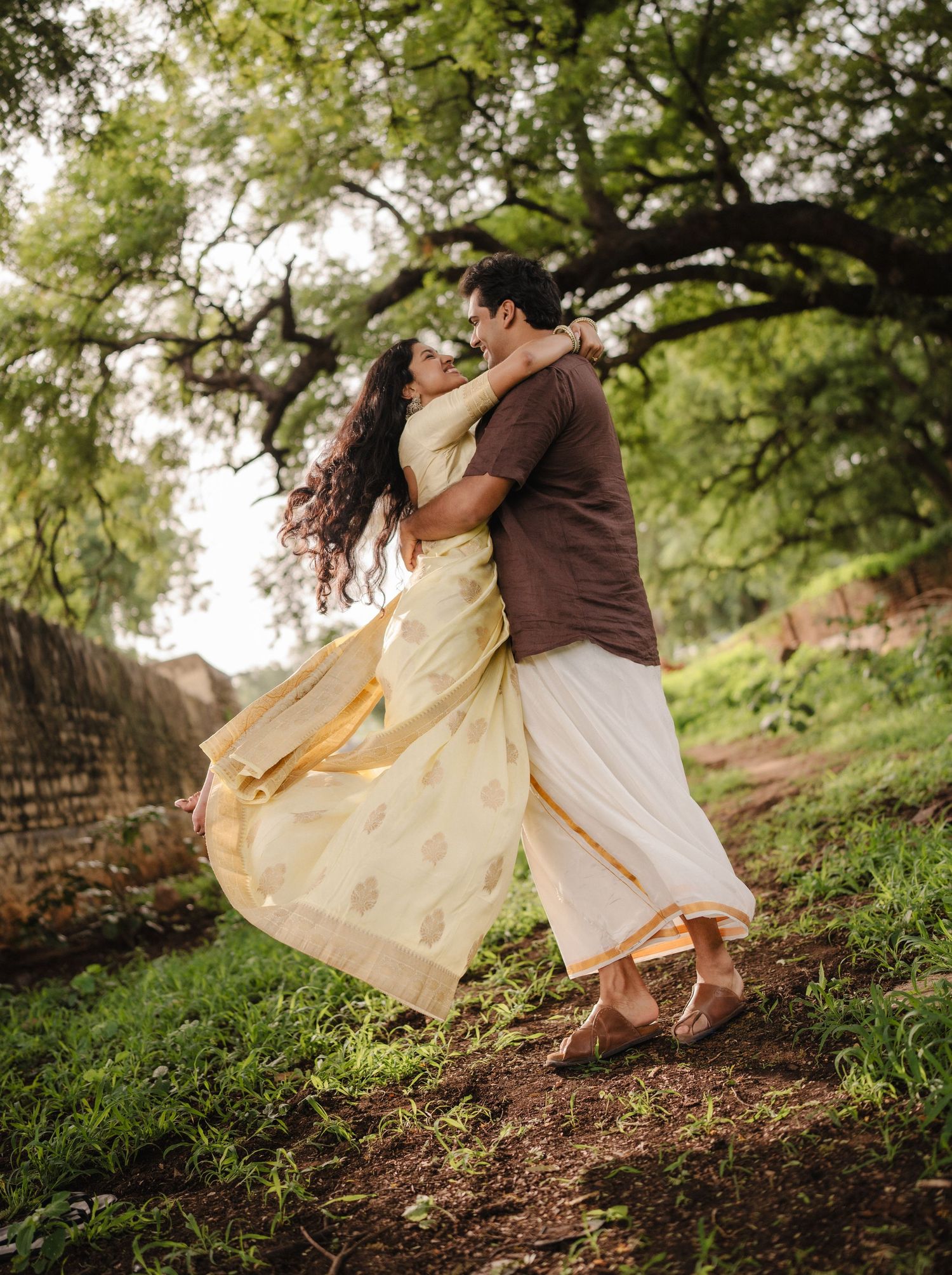 Couple posing at an ancient South Indian stone temple with intricate carvings and a tiered gopuram tower.