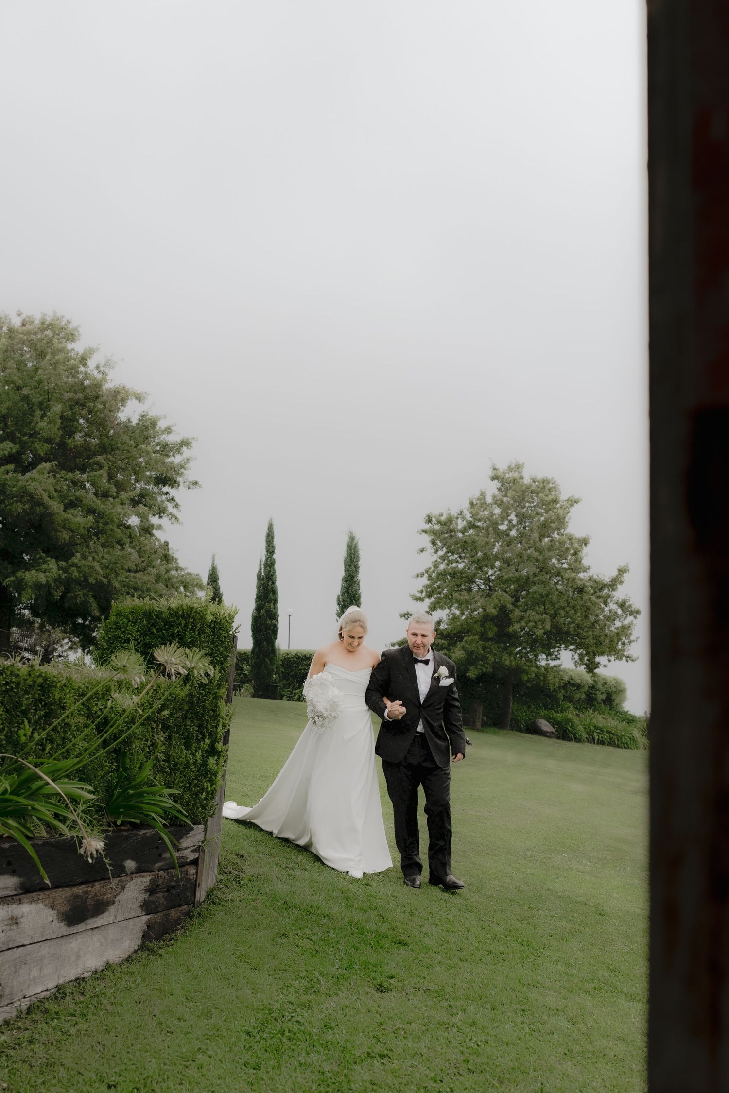 Bride and groom walking arm in arm on lush green lawn surrounded by trees on their wedding day.