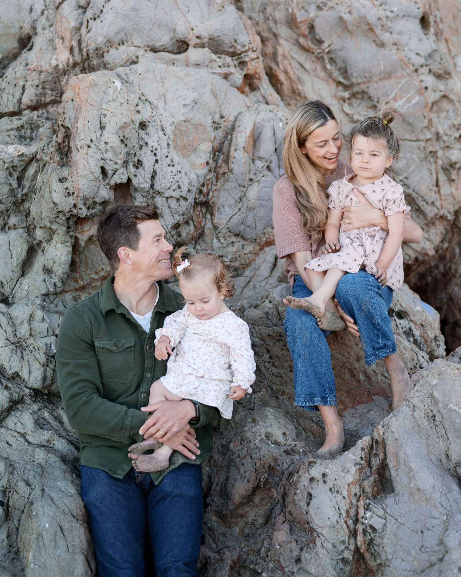 Happy family of four walking hand-in-hand through a lush green park on a sunny day.