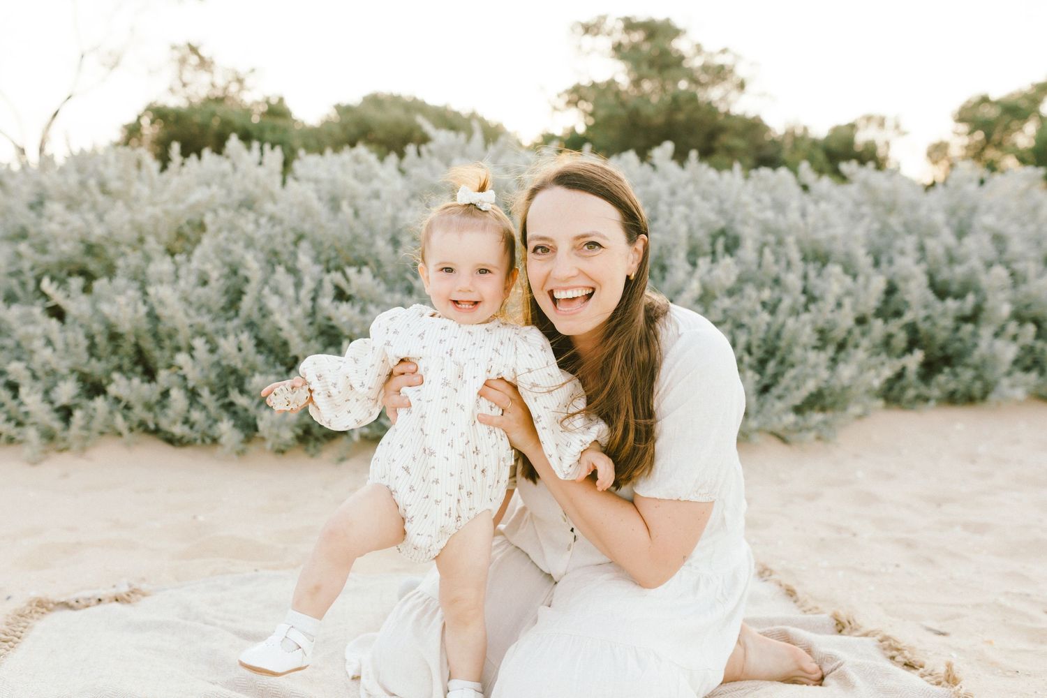 Mother and daughter share joyful moments in a sun-drenched field with sage brush and desert plants.