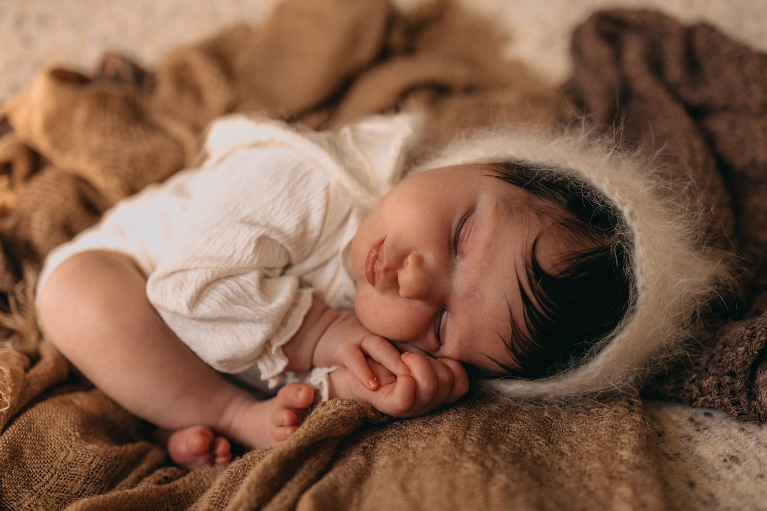 Sleeping newborn curled up on brown fabric in artistic pose.