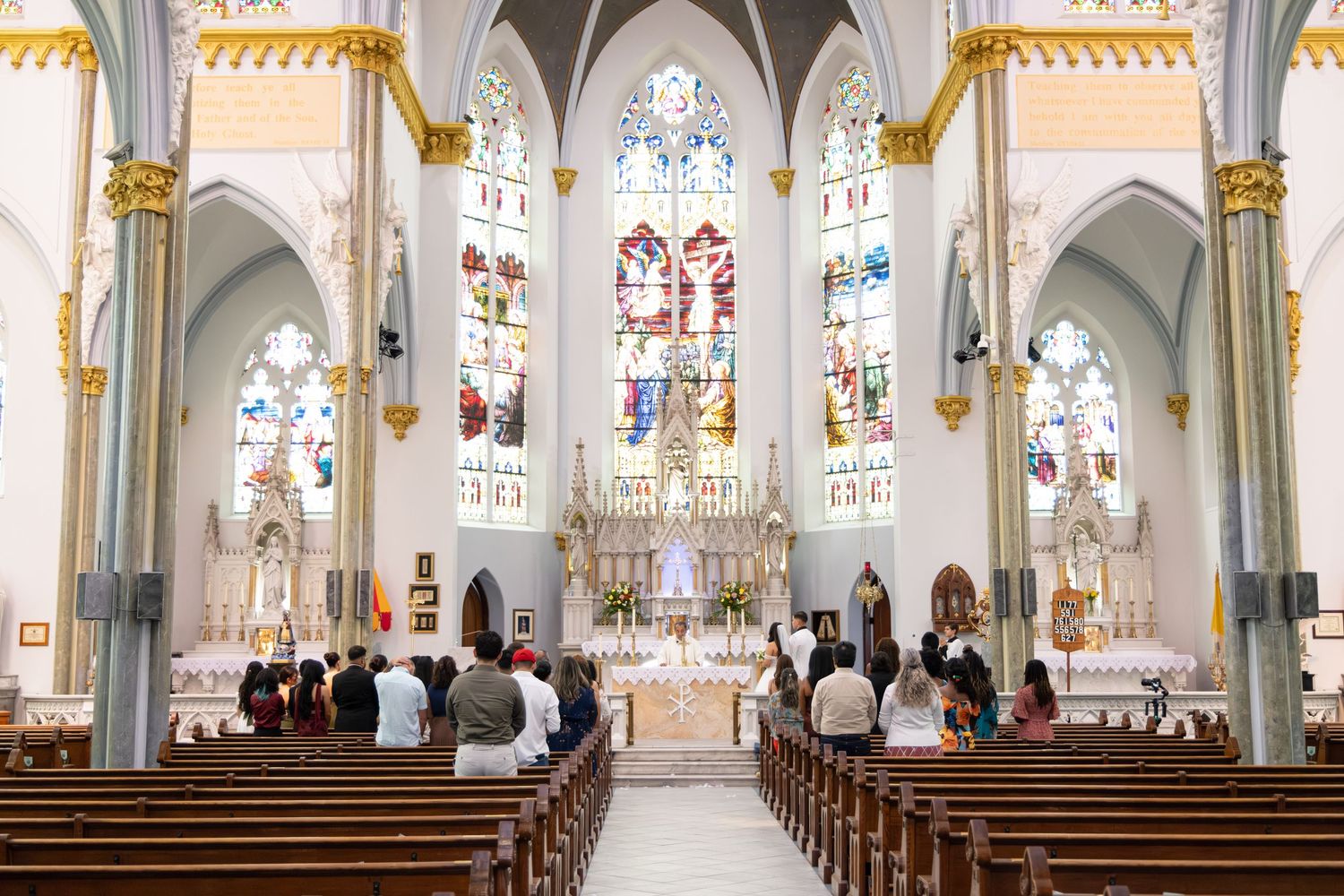 Interior view of a Gothic-style church with ornate columns, stained glass windows, and white vaulted ceilings.