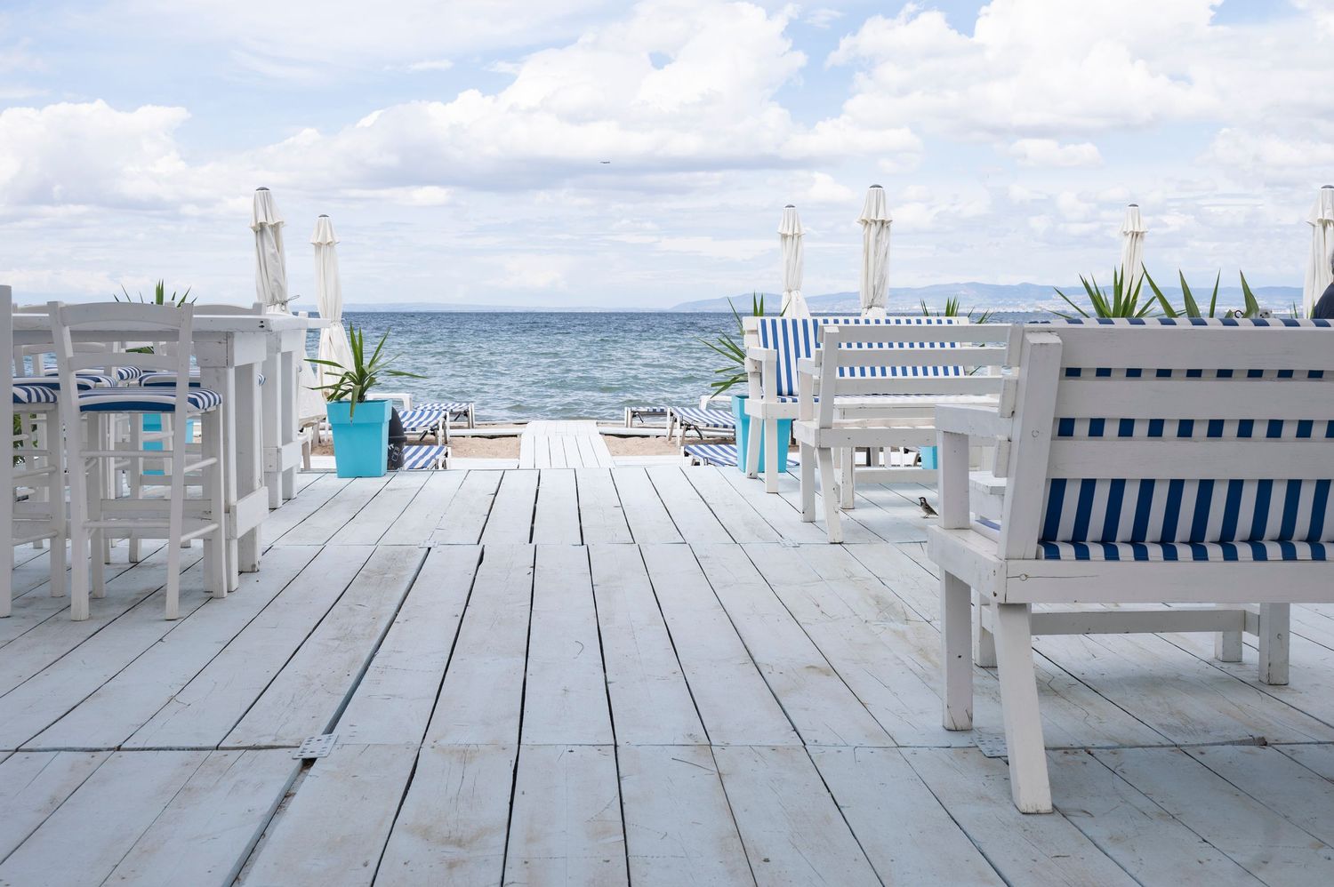 A series of wooden deck chairs and benches arranged along a beachfront boardwalk with ocean views.