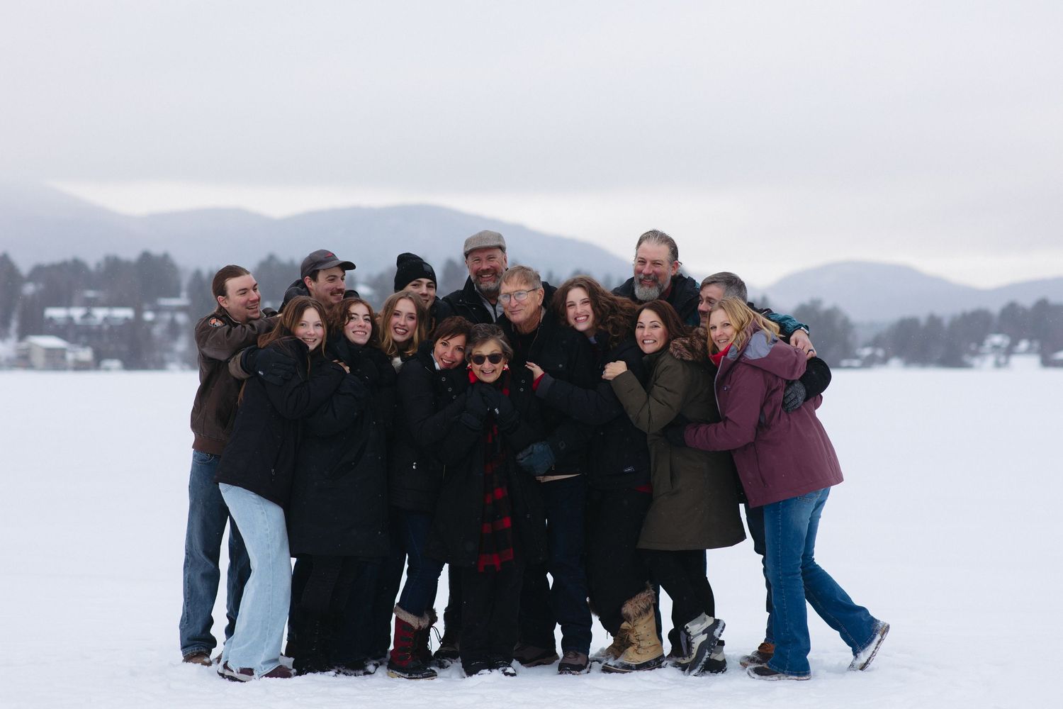 A group of people bundled in winter coats pose together on a snowy landscape with mountains in the background.