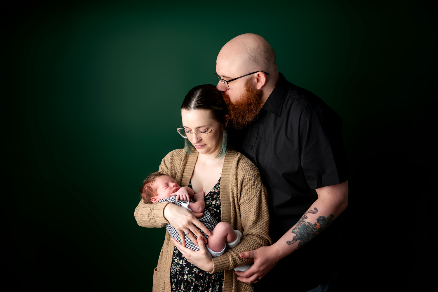 New parents tenderly holding their newborn baby against a dark green studio background.