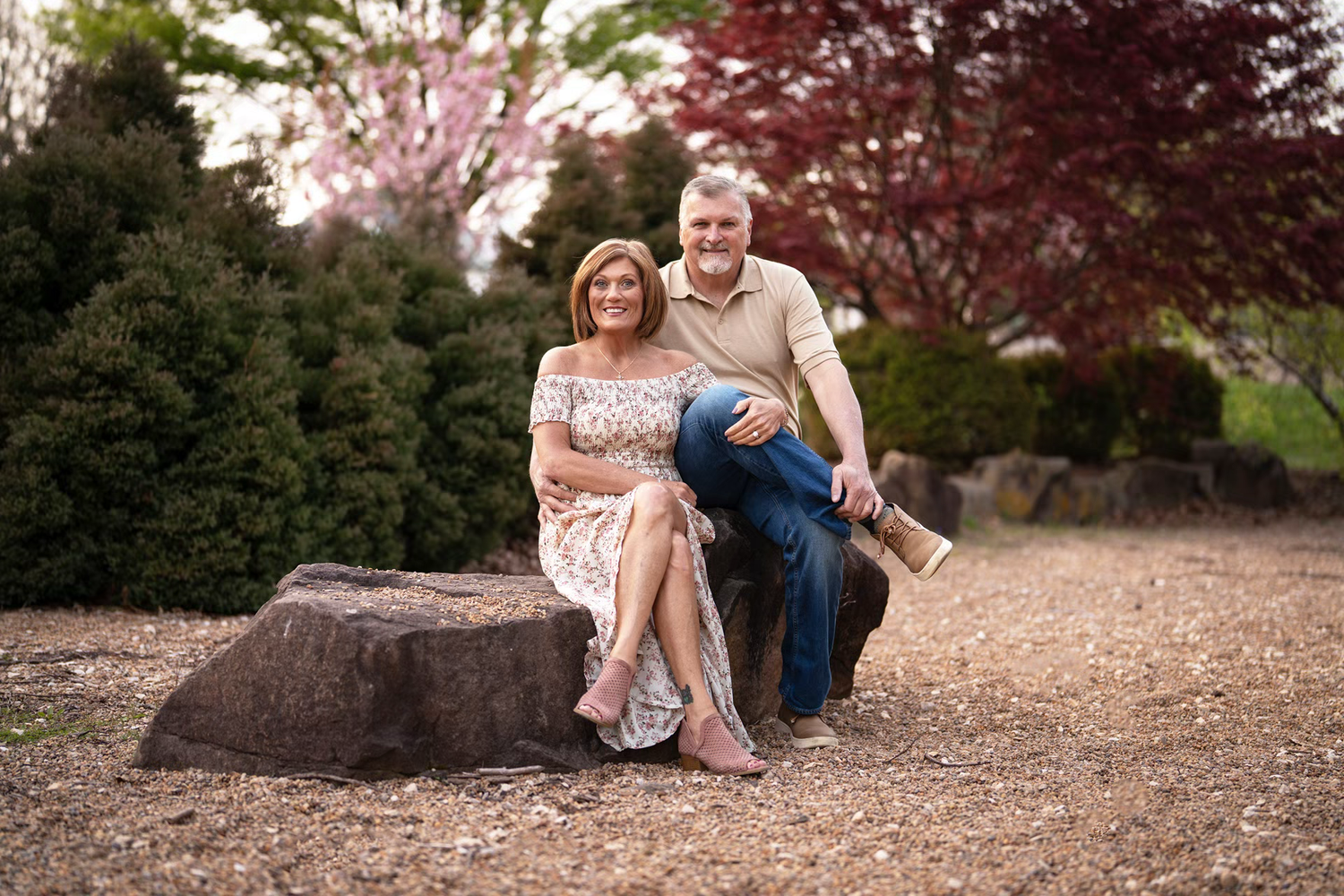 A smiling couple poses together on a large rock in Franklin Park Conservatory Engagement Photos