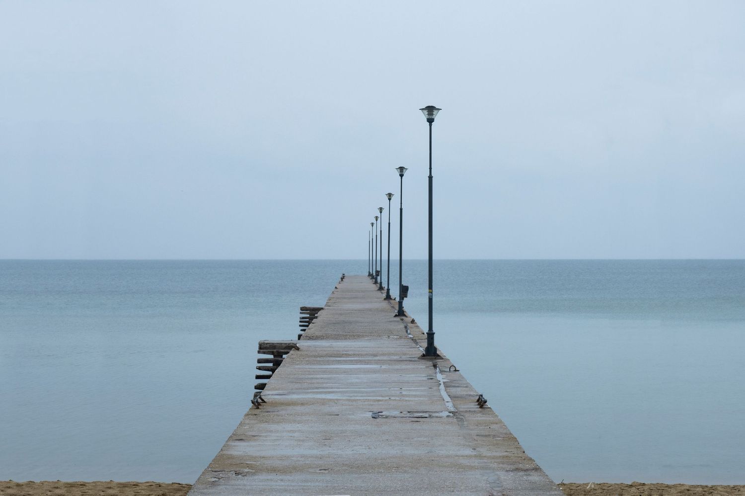 A long wooden pier extends into the calm blue ocean waters under an overcast sky at dusk.