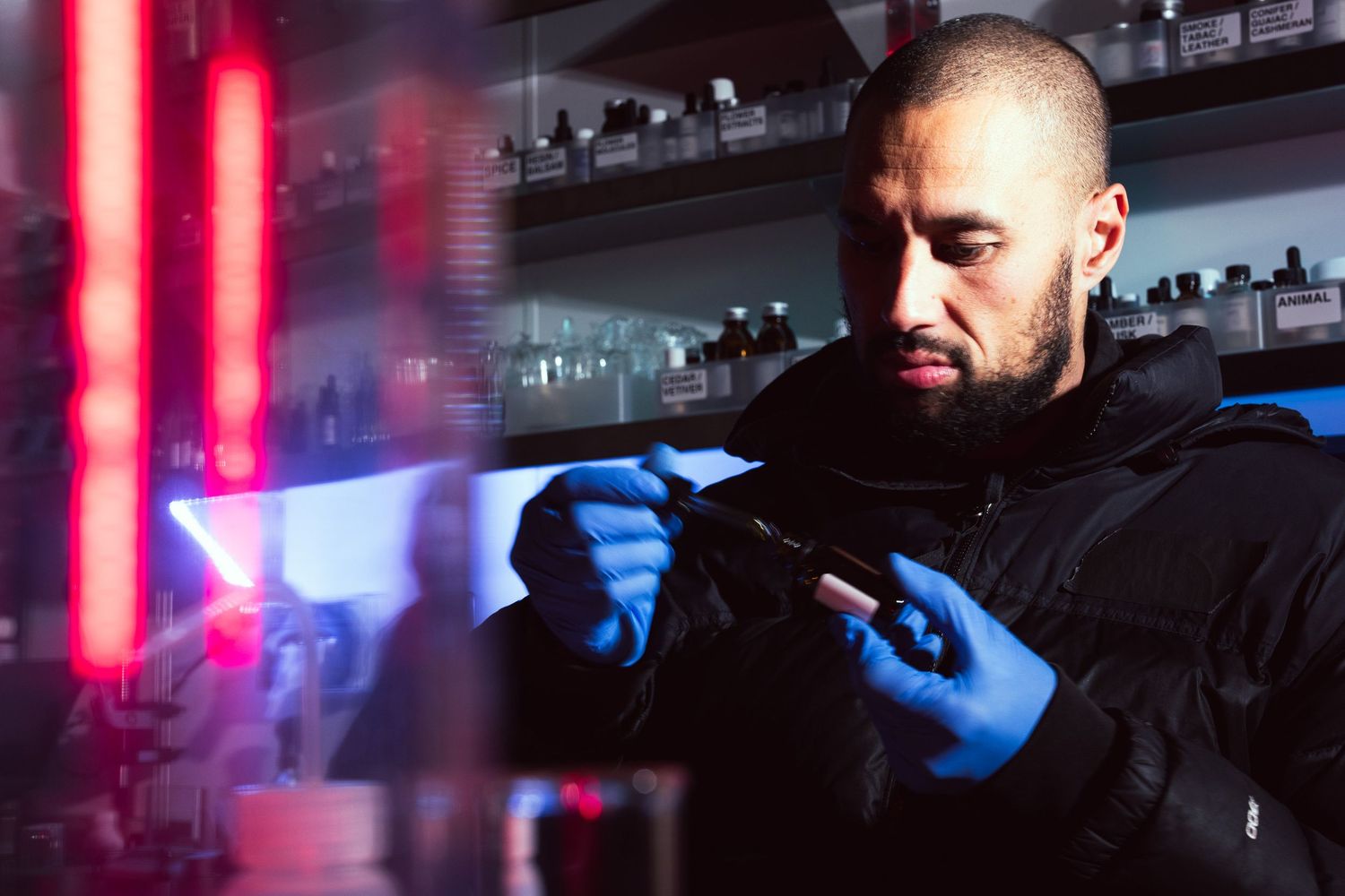 A darkly lit image with moody red and blue light of Nathan Taare blends oils to create a new perfume