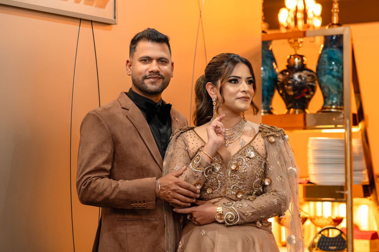 Elegant couple posing together, man in brown suit, woman in gold embroidered gown, at a formal event.